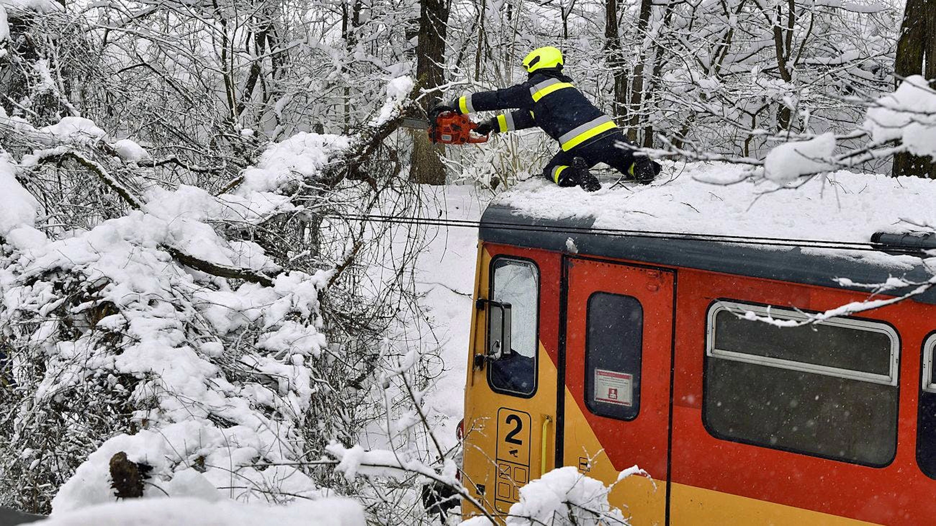 Galionsfigur mit Kettensäge: Im ungarischen Szilvásvárad streckt sich ein Feuerwehrmann auf dem Dach eines Zugs, um einen Ast abzusägen, der unter der Schneelast heruntergebrochen ist und die Bahnstrecke blockiert. (25.1.2021)