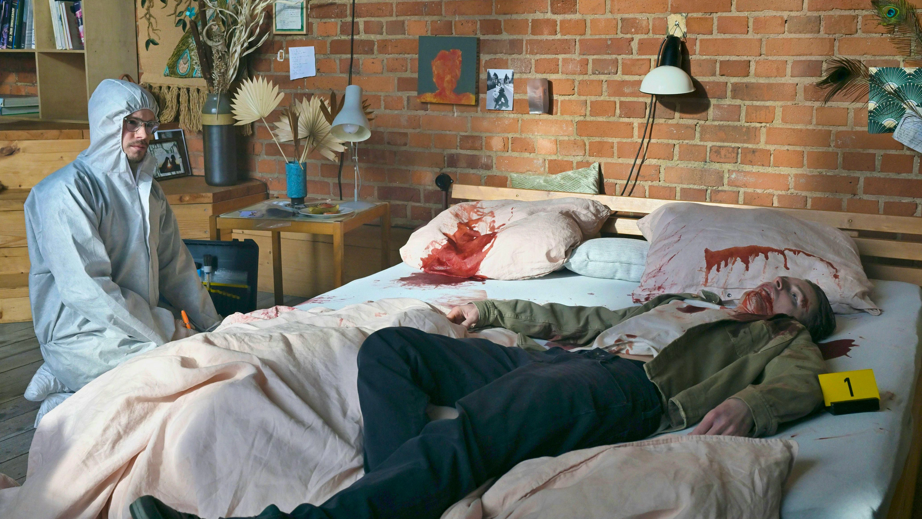 Dr. Jonathan Himpe (Ron Helbig, links) untersucht den Tatort. David Konradt (Frederik Bechtle), der Freund der Tatverdächtigen, wurde im Bett erstochen.