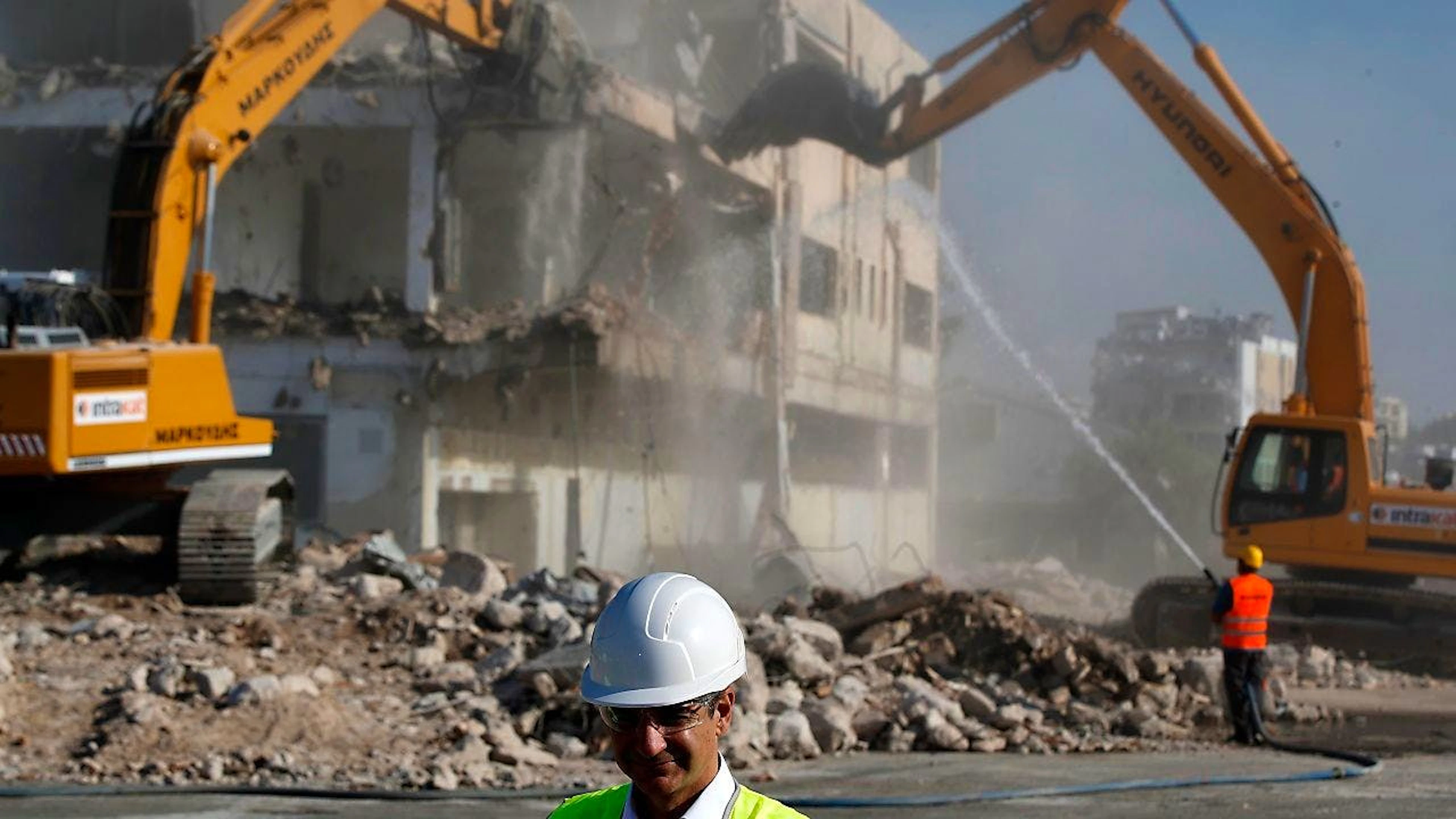 ARCHIV - Kyriakos Mitsotakis, Premierminister von Griechenland, mit Helm und Kunststoffbrille auf dem alten Flughafen, während Bulldozer ein verlassenes Gebäude abreißen. Foto: Thanassis Stavrakis/AP/dpa