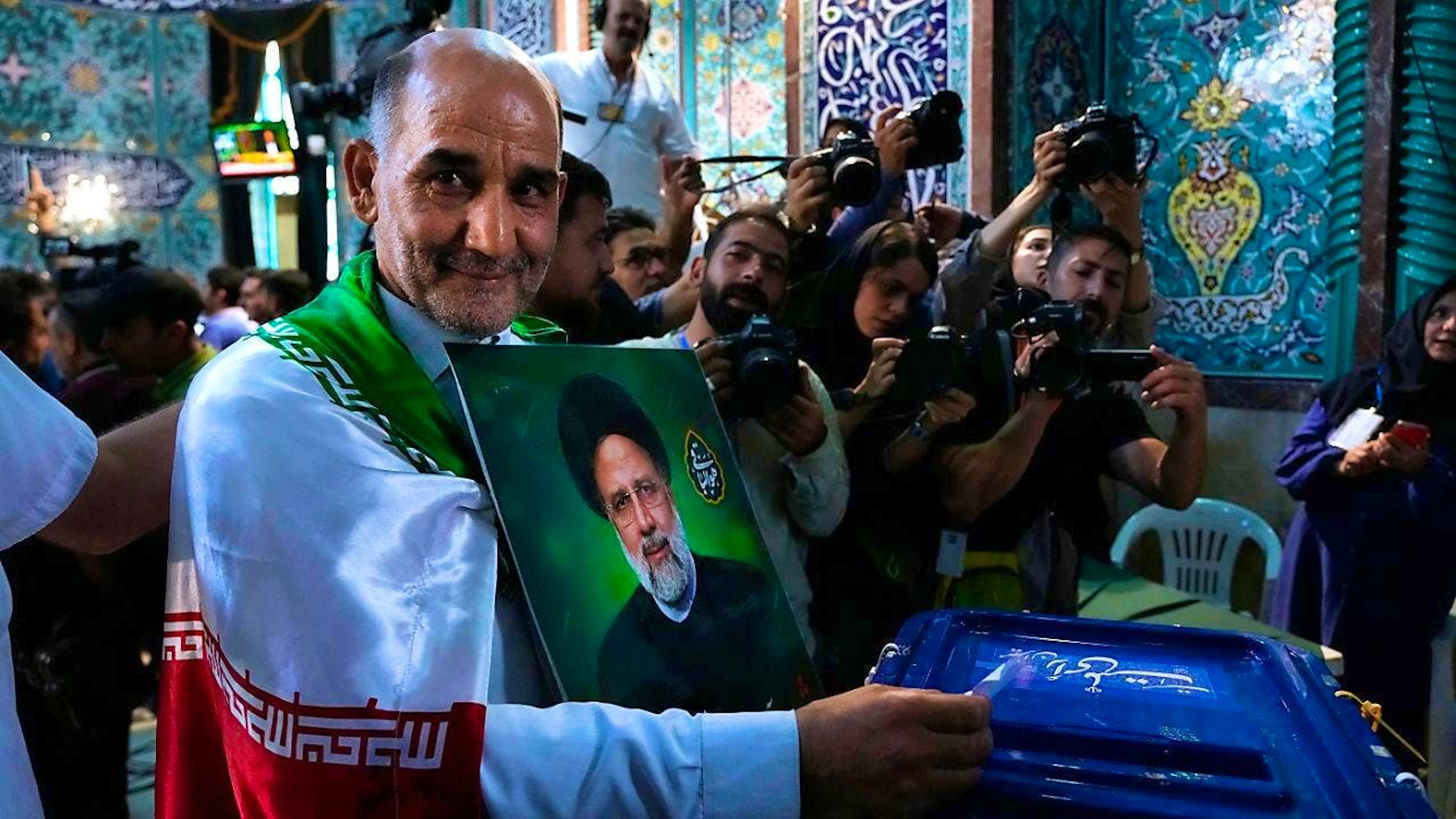 dpatopbilder - A man casts his vote during the presidential election while holding a picture of the late President Ebrahim Raisi at a polling station. Around 61 million voters in the Islamic Republic are called upon to elect a new head of government. Photo: Vahid Salemi/AP