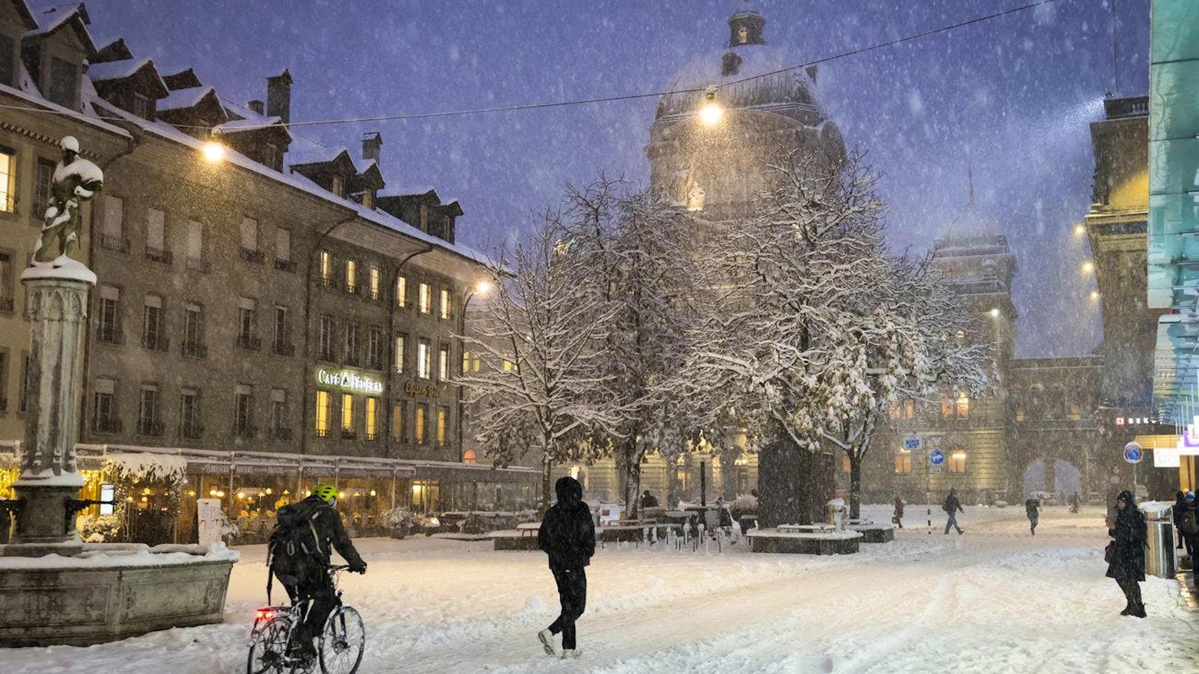 Des passants marchent et font du vélo dans la neige sur la Baerenplatz devant le Palais fédéral, le jeudi 21 novembre 2024 à Berne. (KEYSTONE/Peter Klaunzer)