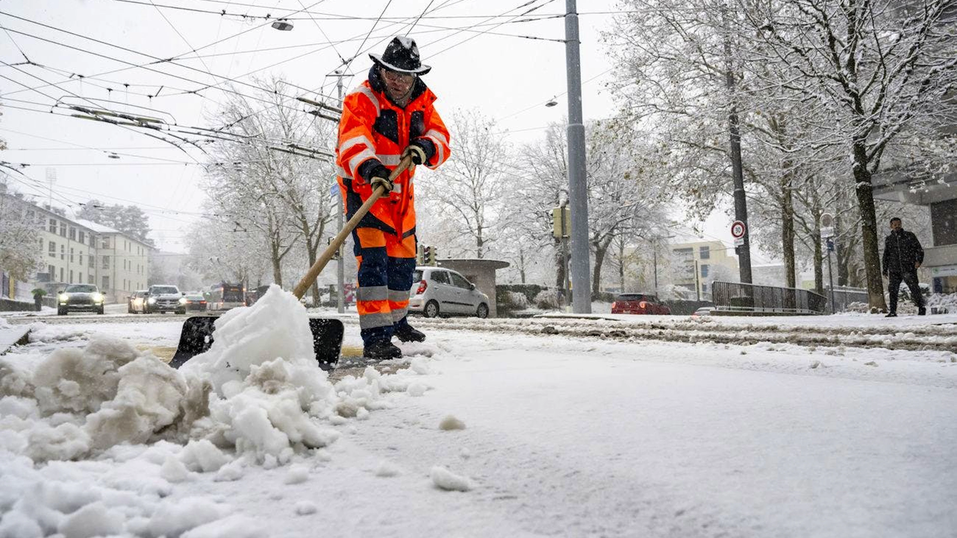 Un employé de la voirie de la ville de Lausanne enlève la neige sur la chaussée avec une pelle lors des chutes de neige le jeudi 21 novembre 2024 à Lausanne. (KEYSTONE/Jean-Christophe Bott)