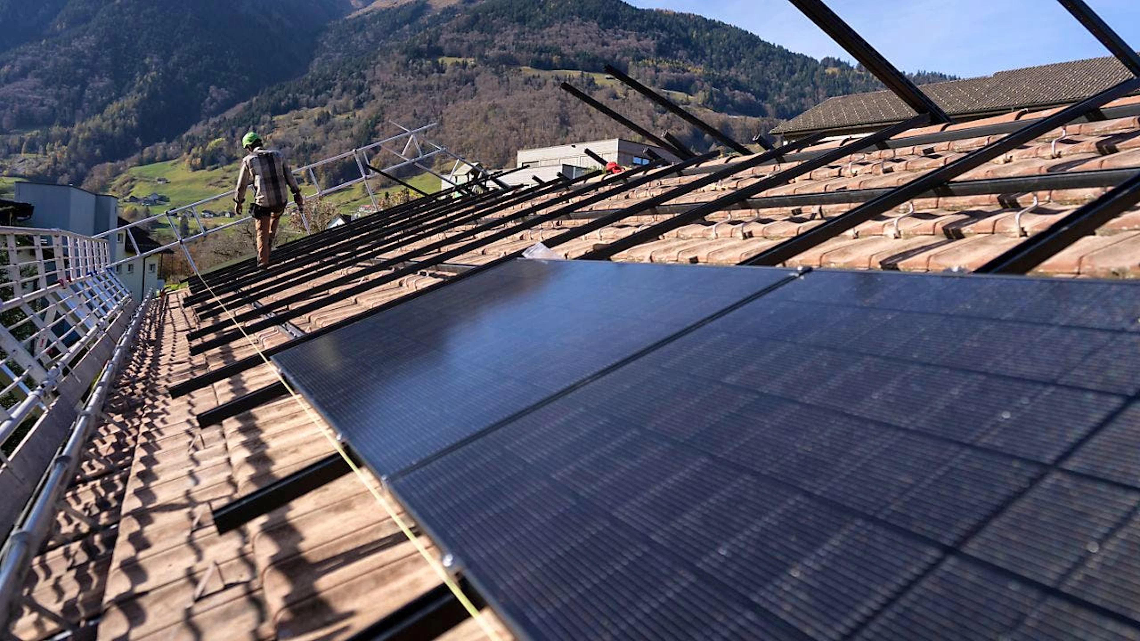 Solarinstallateure befestigen die Solarpaneele auf dem Dach eines Hauses. Im Kanton Bern entscheiden die Stimmberechtigten im Februar über eine flächendeckende Solarpflicht.