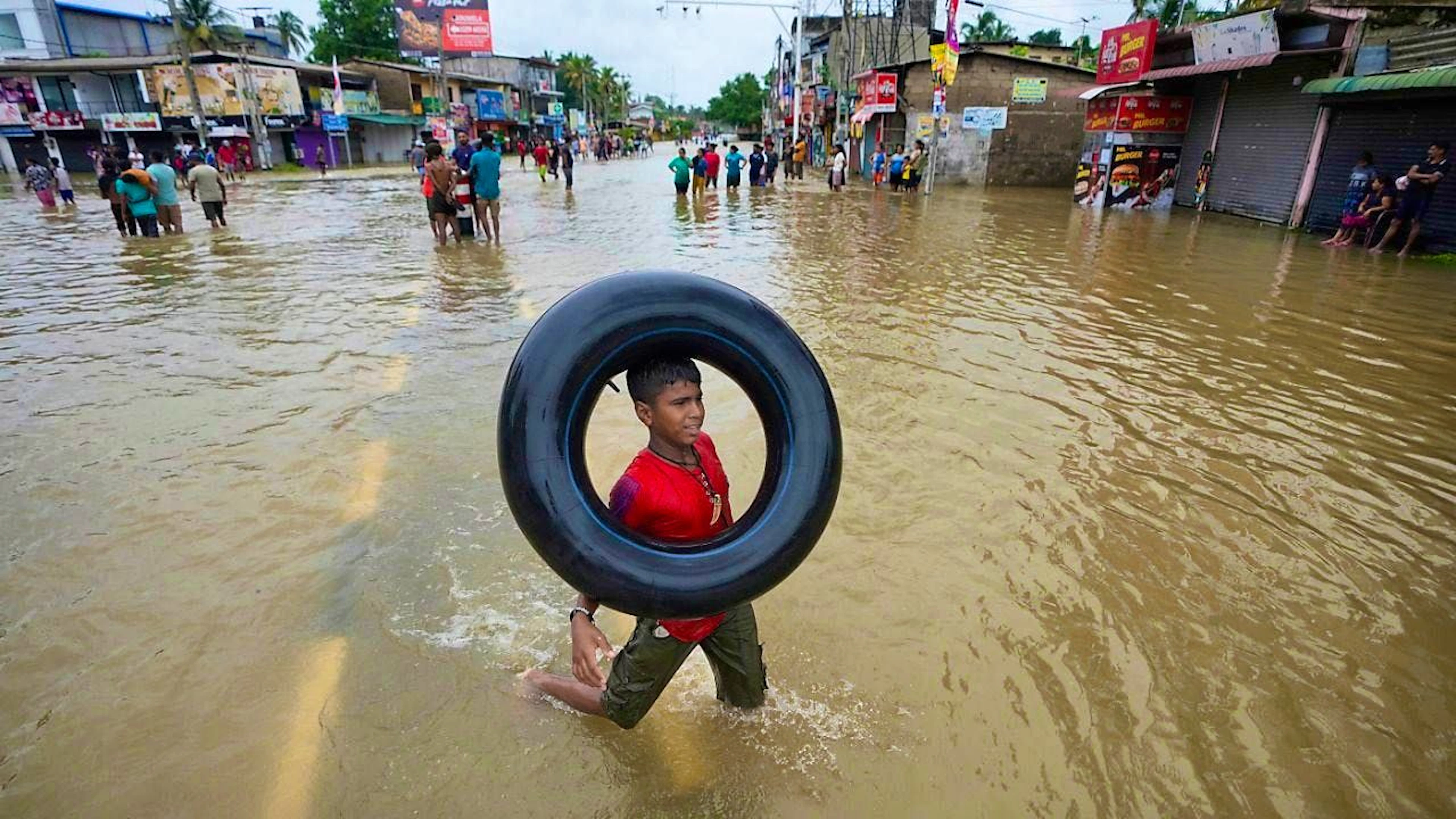 ARCHIVE - A boy plays with an inflatable rubber tube in a flooded street in Biyagama, a suburb of Colombo. Schools were closed in Sri Lanka on Monday (03.06.2024) as heavy rains triggered flooding and mudslides in many parts of the island nation, killing at least ten people and leaving six others missing, authorities said. Photo: Eranga Jayawardena/AP/dpa