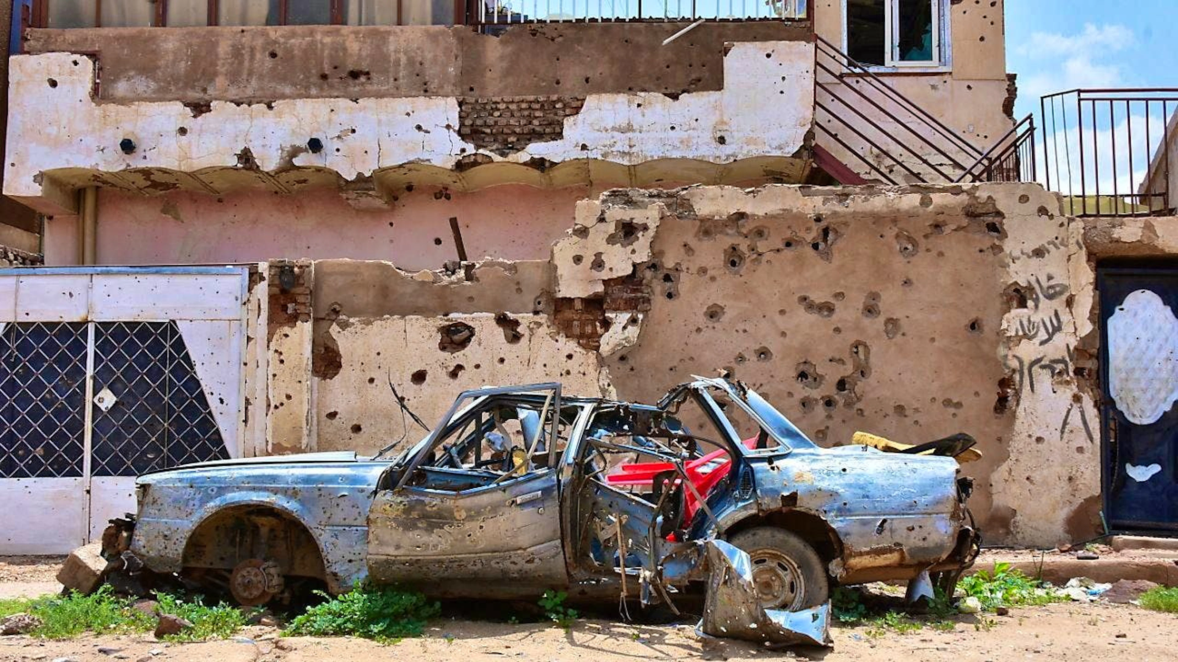ARCHIVE - A destroyed car stands in front of a house full of bullet holes in Omdurman, Sudan. Photo: Mudathir Hameed/dpa/Archive picture