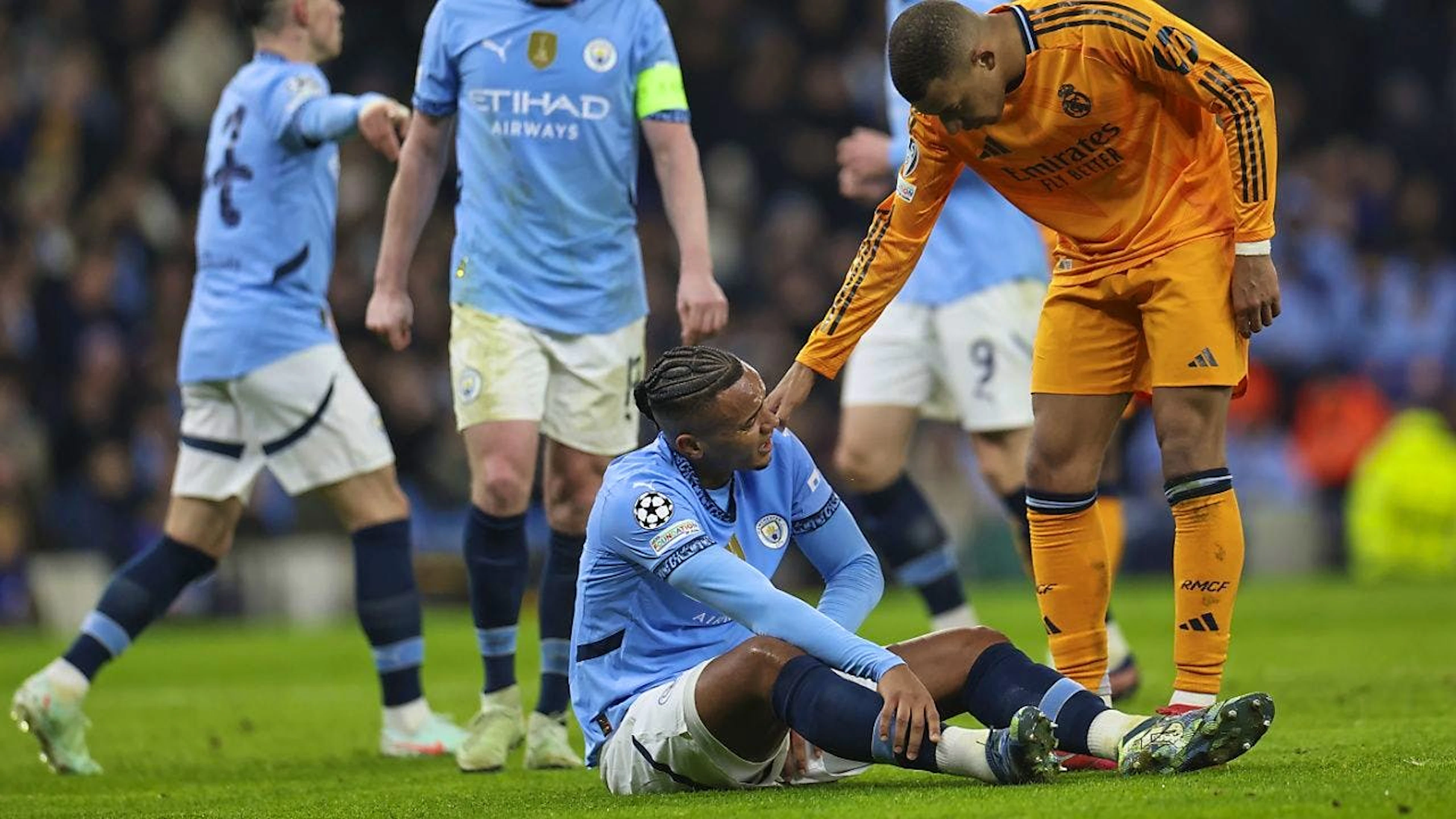 Real Madrids Kylian Mbappé (rechts) erkundigt sich bei Manchester Citys Verteidiger Manuel Akanji (am Boden sitzend) nach dem Befinden.
