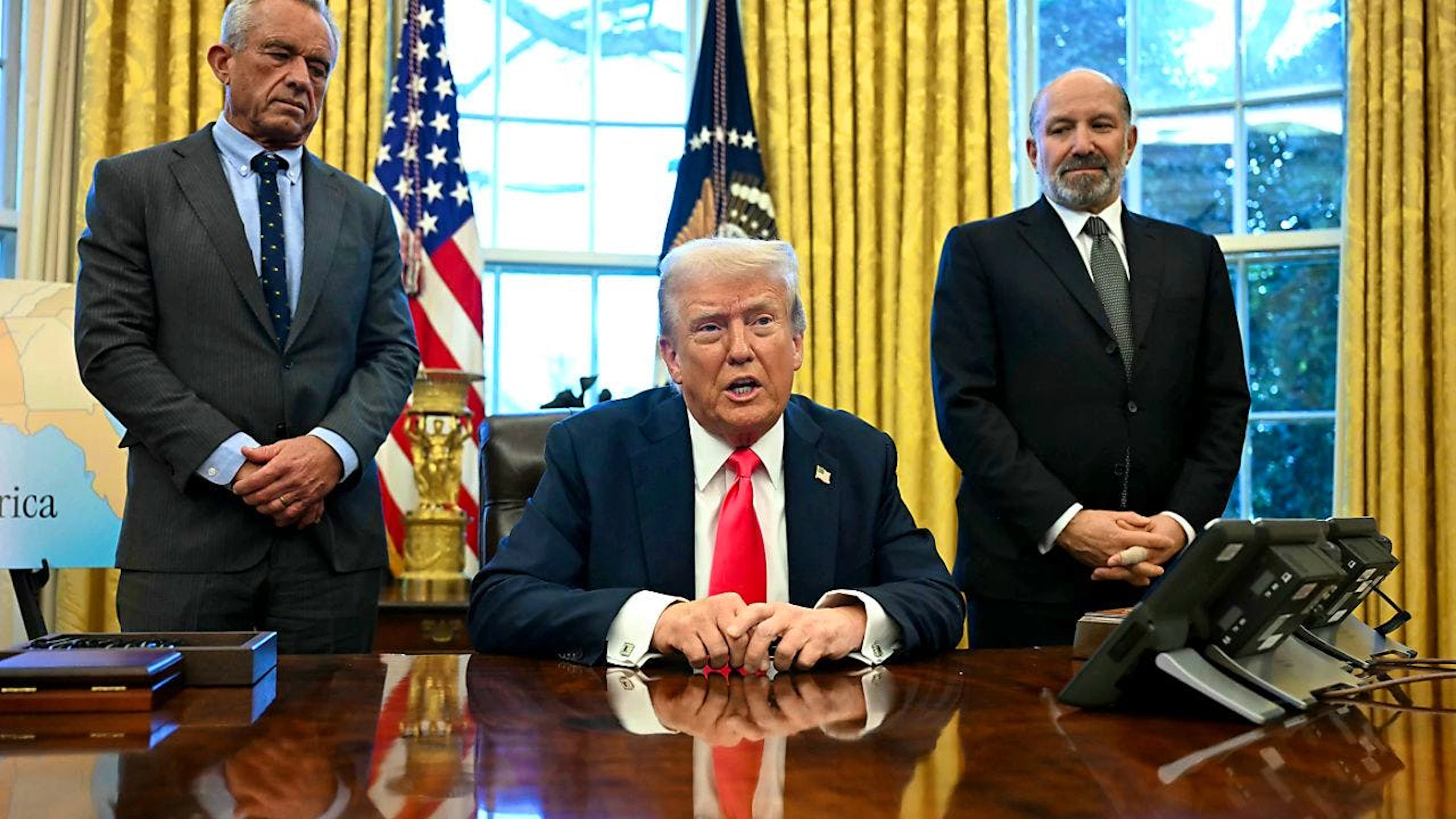US-Präsident Donald Trump spricht zu Reportern, bevor er eine Anordnung unterzeichnet, während Gesundheitsminister Robert F. Kennedy Jr. (l) und Handelsminister Howard Lutnick im Oval Office des Weißen Hauses zuhören. Foto: Uncredited/Pool/AP/dpa