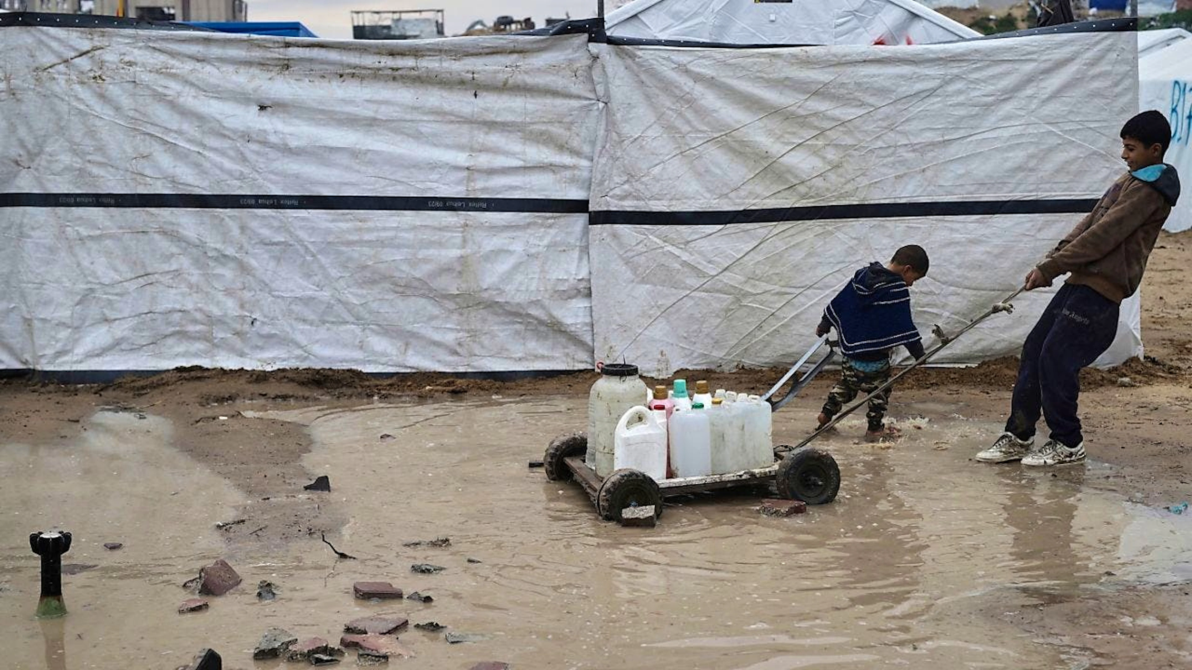 Ein Junge und ein Kind ziehen Wasser in Plastikkanistern in einem Zeltlager für vertriebene Palästinenser, deren Häuser durch Angriffe der israelischen Armee zerstört wurden. Foto: Jehad Alshrafi/AP/dpa