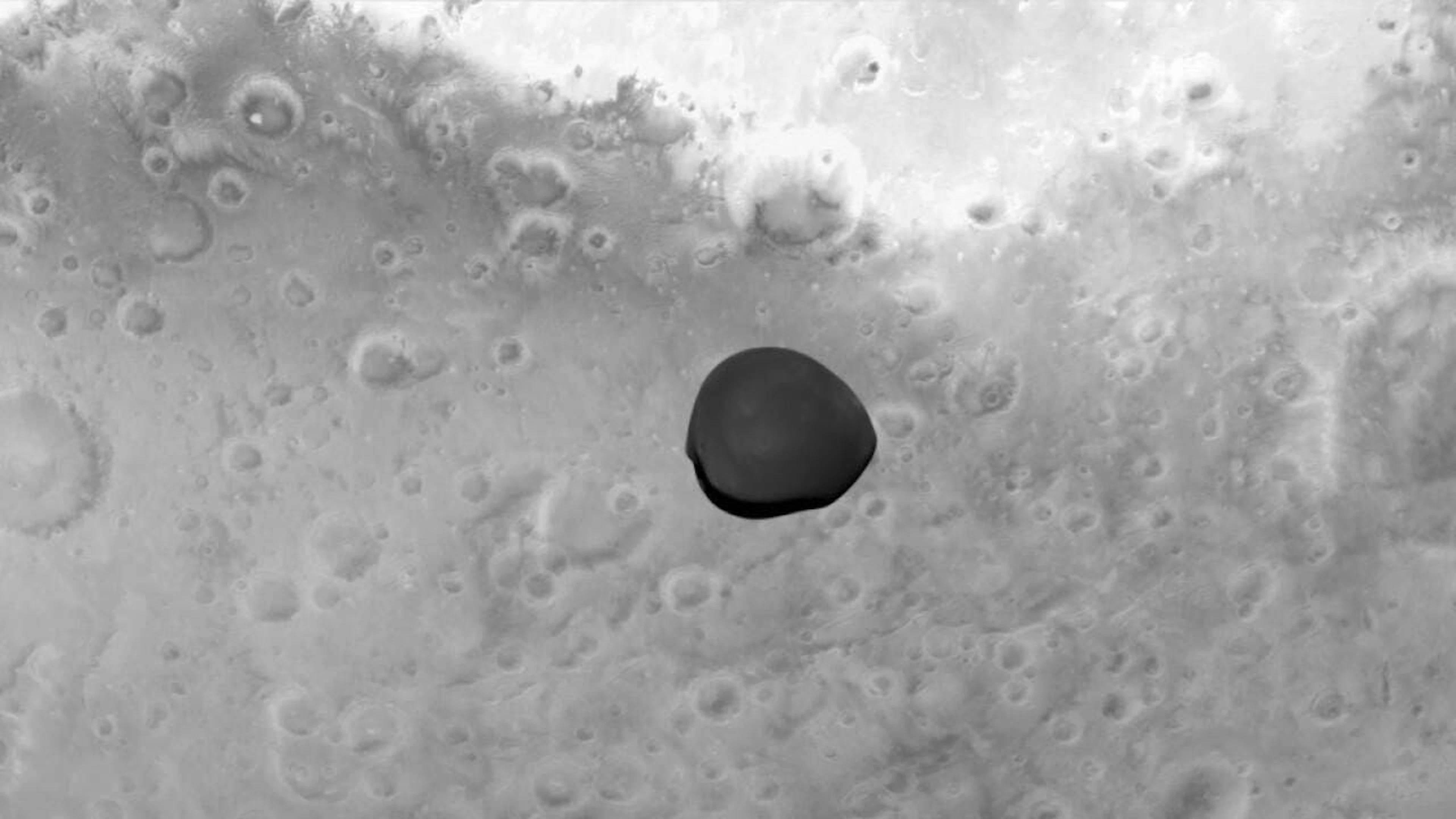 Dieses Bild des Marsmondes Deimos wurde am 12. März von der ESA-Raumsonde Hera während ihres Vorbeiflugs am Mars aufgenommen. Der im Hintergrund sichtbare Planet ist der Mars.