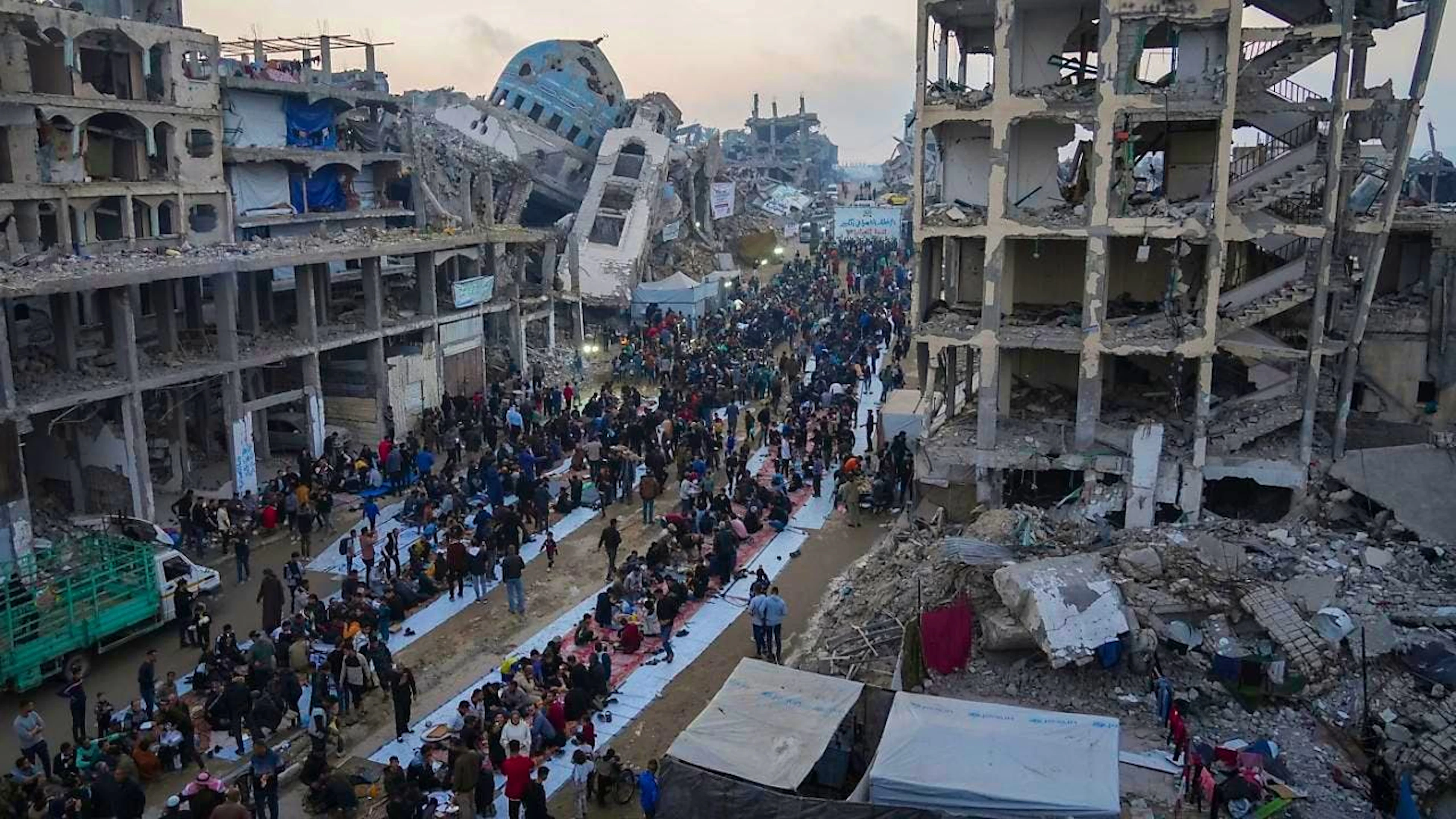 Umgeben von zerstörten Häusern und Gebäuden versammeln sich Palästinenser zum Iftar, dem Fastenbrechen während des Ramadan, in Beit Lahia im nördlichen Gazastreifen. Foto: Jehad Alshrafi/AP/dpa