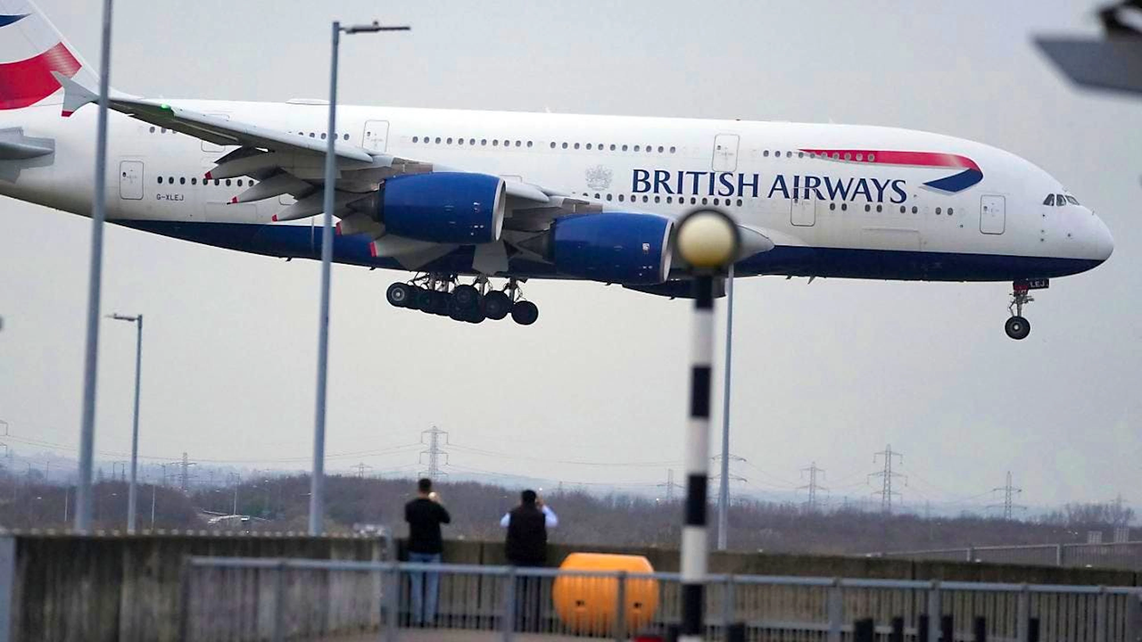 Menschen beobachten die Landung eines Flugzeugs der British Airways, während die Behörden die teilweise Wiederaufnahme des Flugbetriebs ankündigen, nachdem ein Brand in einem nahe gelegenen Umspannwerk zur Schließung des verkehrsreichsten Flughafens Europas geführt hat. Foto: Kin Cheung/AP/dpa
