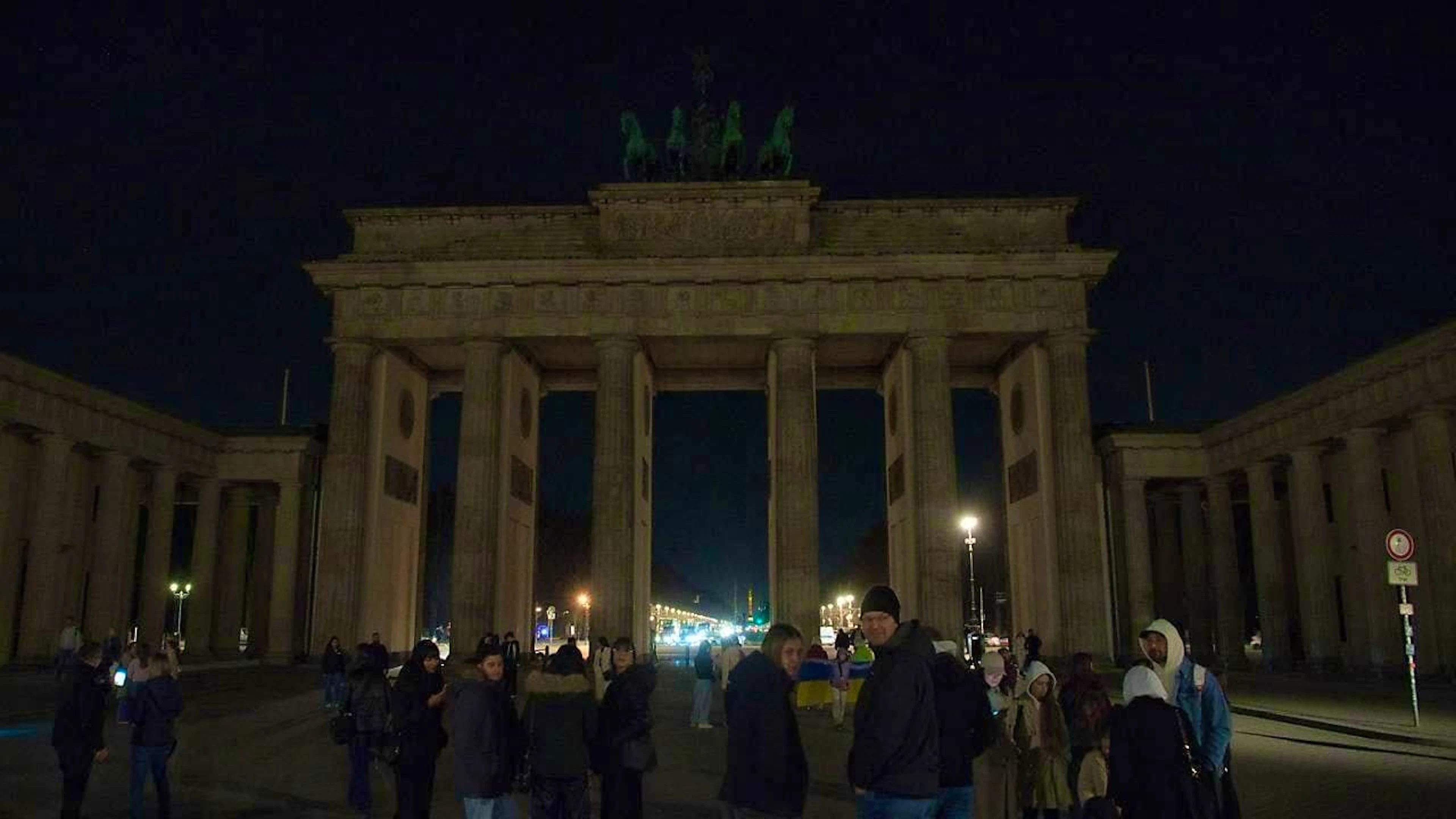dpatopbilder - People stand in front of the dark Brandenburg Gate. With the worldwide "Earth Hour" campaign, the environmental protection organization WWF wants to set an example for more climate protection. Photo: Paul Zinken/dpa