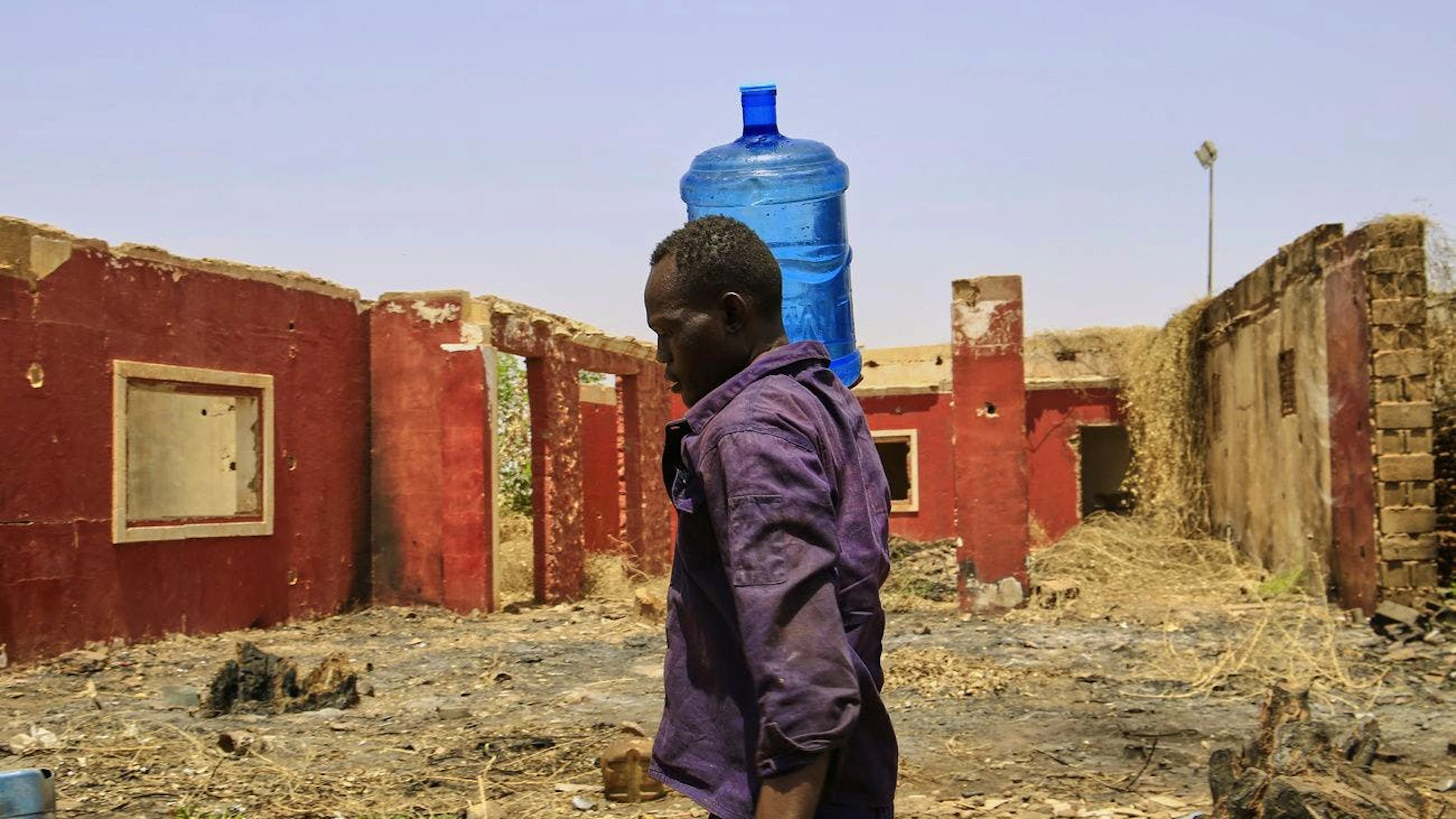Un homme porte un récipient d'eau devant un bâtiment endommagé pendant la guerre civile à un point de distribution en raison de coupures d'eau à Khartoum, au Soudan, le dimanche 25 mai 2025. 