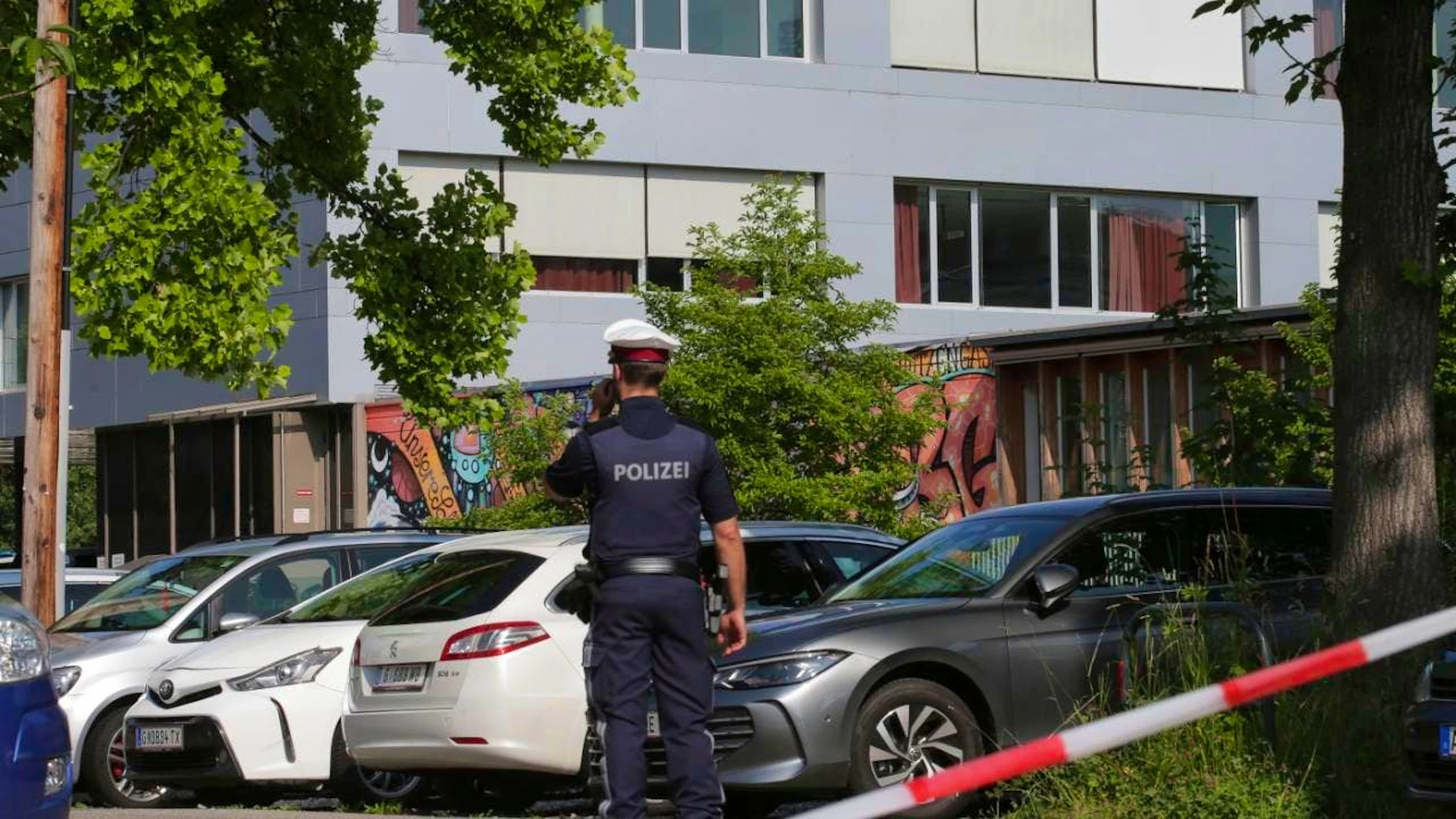 Ein Polizeibeamter telefoniert vor dem Schulgebäude. Ein 21-Jähriger aus dem Raum Graz hat nach Angaben der Behörden die tödlichen Schüsse an einem Gymnasium im österreichischen Graz abgegeben. Am Vormittag hatte der Mann neun Menschen getötet und danach Suizid begangen. Foto: Heinz-Peter Bader/AP/dpa