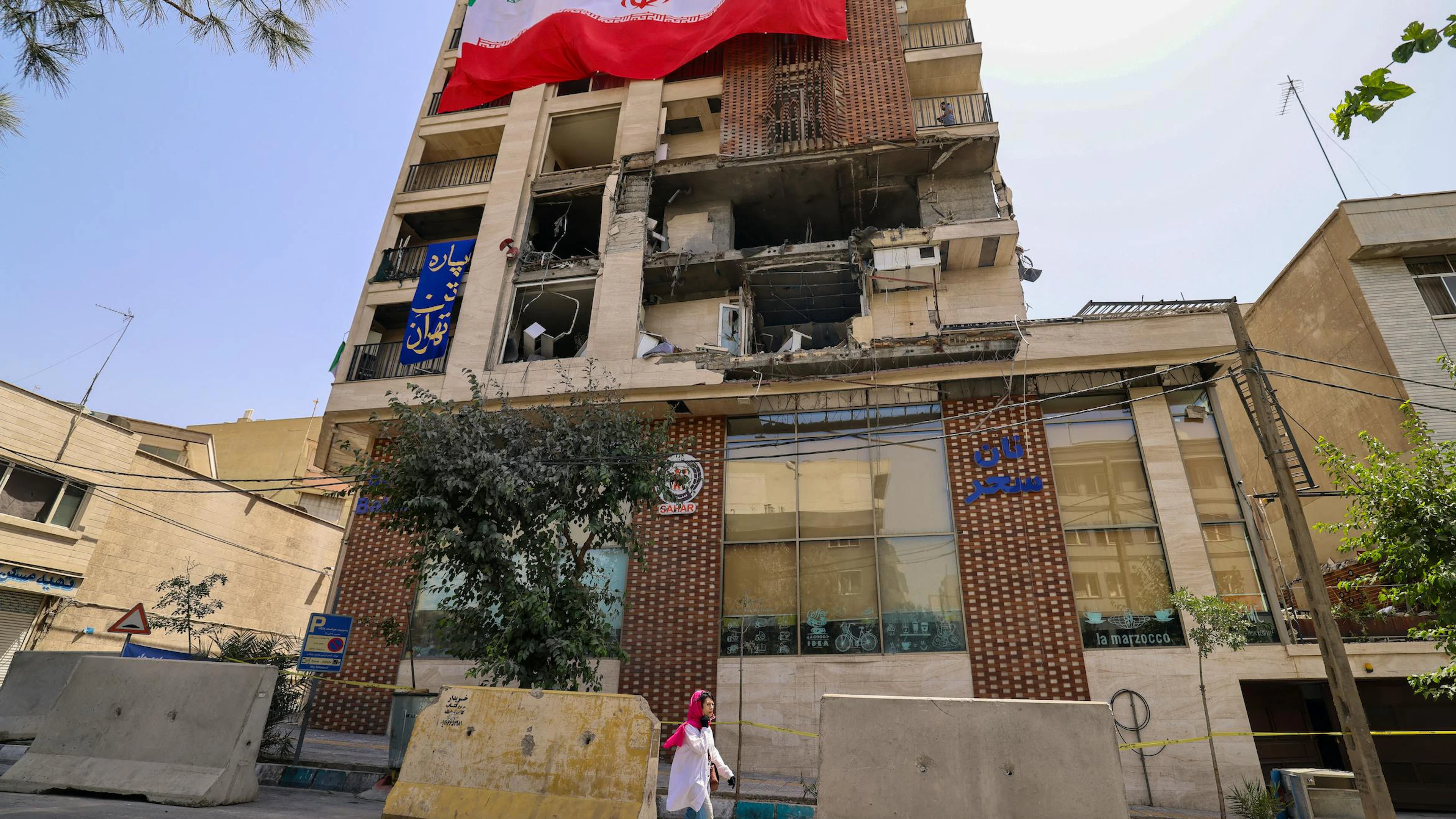 Une femme passe devant un immeuble résidentiel touché par une frappe israélienne et recouvert d'un grand drapeau iranien, à Téhéran, le 25 juin 2025.