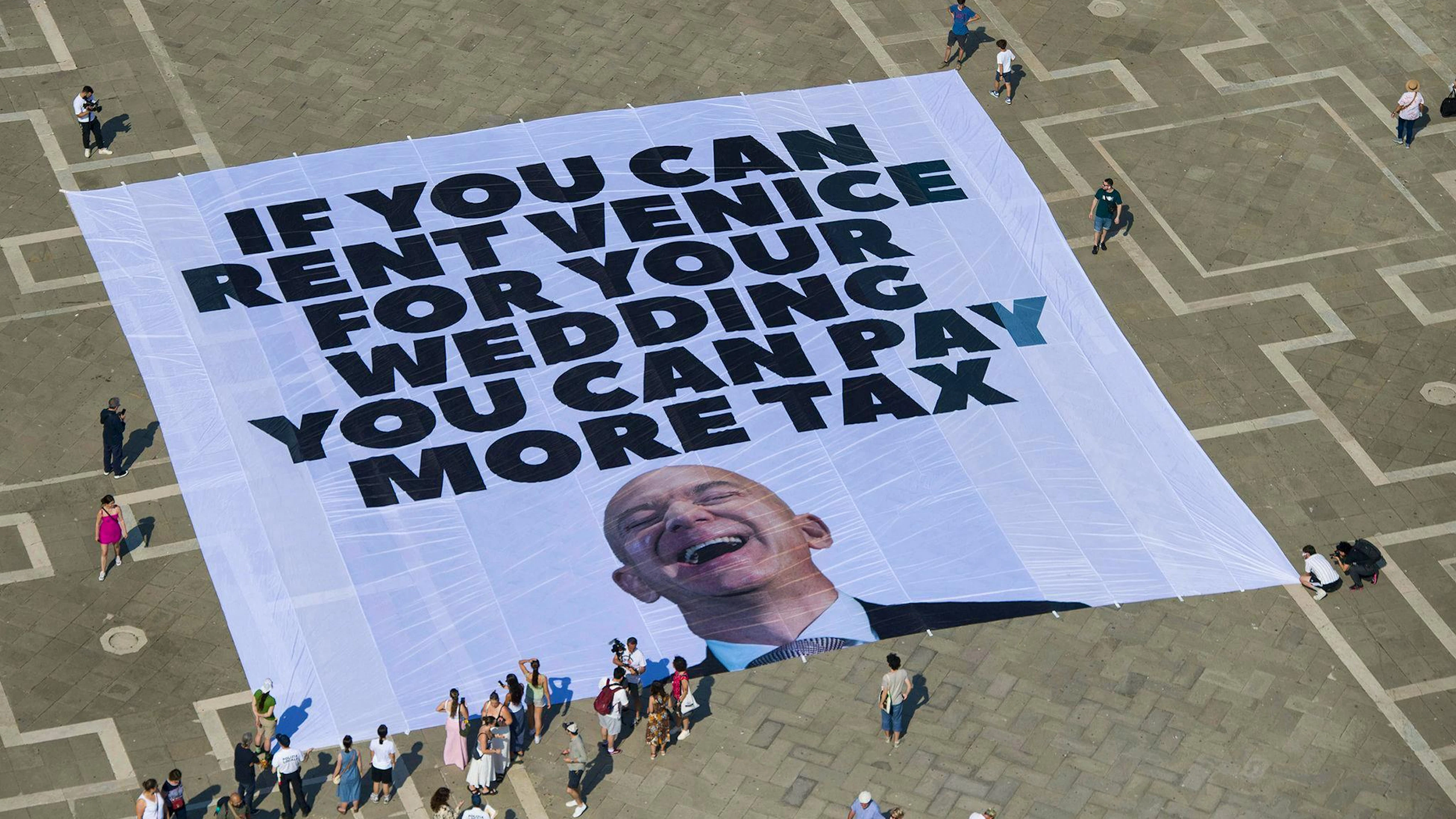 Mit einem Plakat auf dem Markusplatz fordern Greenpeace-Aktivisten, Bezos höher zu besteuern.