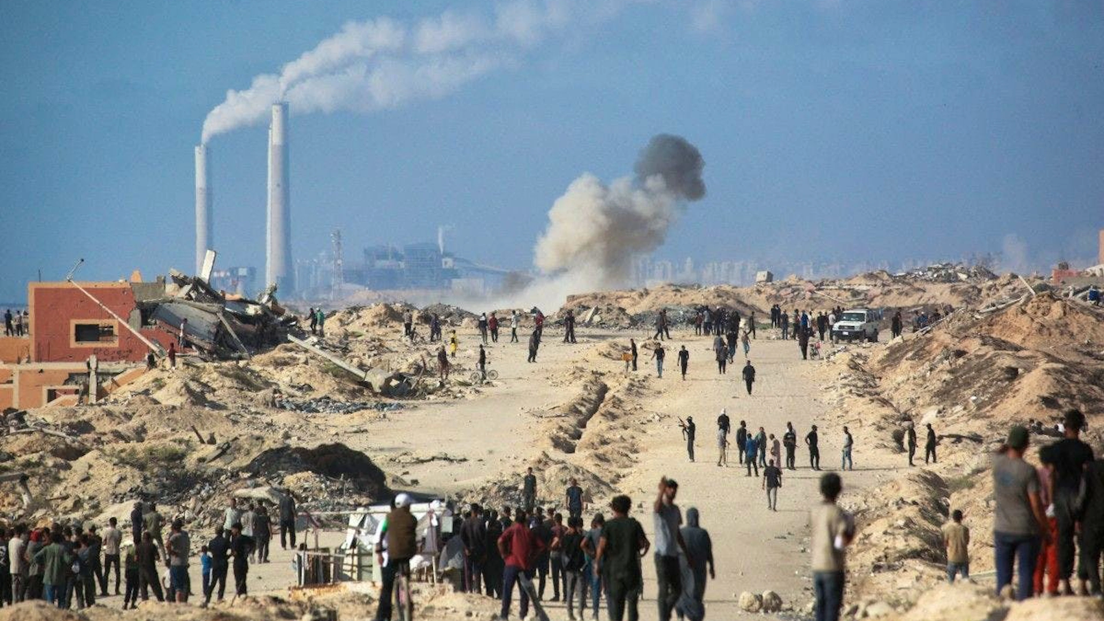 Des déplacés regardent des volontaires issus de familles palestiniennes, organisés en comités pour prévenir les vols, se rassembler autour d’un véhicule de l’ONU escortant des camions d’aide à destination de la bande de Gaza, en provenance du point de passage de Zikim, contrôlé par Israël. Pendant ce temps, de la fumée s’élève à l’ouest de Beit Lahia, dans le nord du territoire palestinien assiégé, après des frappes israéliennes, le 25 juin 2025.