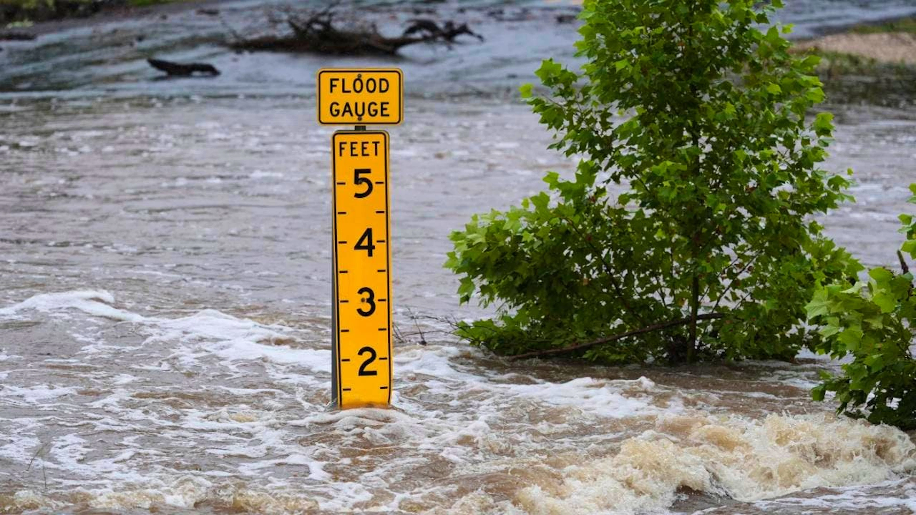 Ein Pegelmesser zeigt die Höhe des Wassers an, das über einer Landstraße in der Nähe von Kerrville fließt. Foto: Eric Gay/AP/dpa