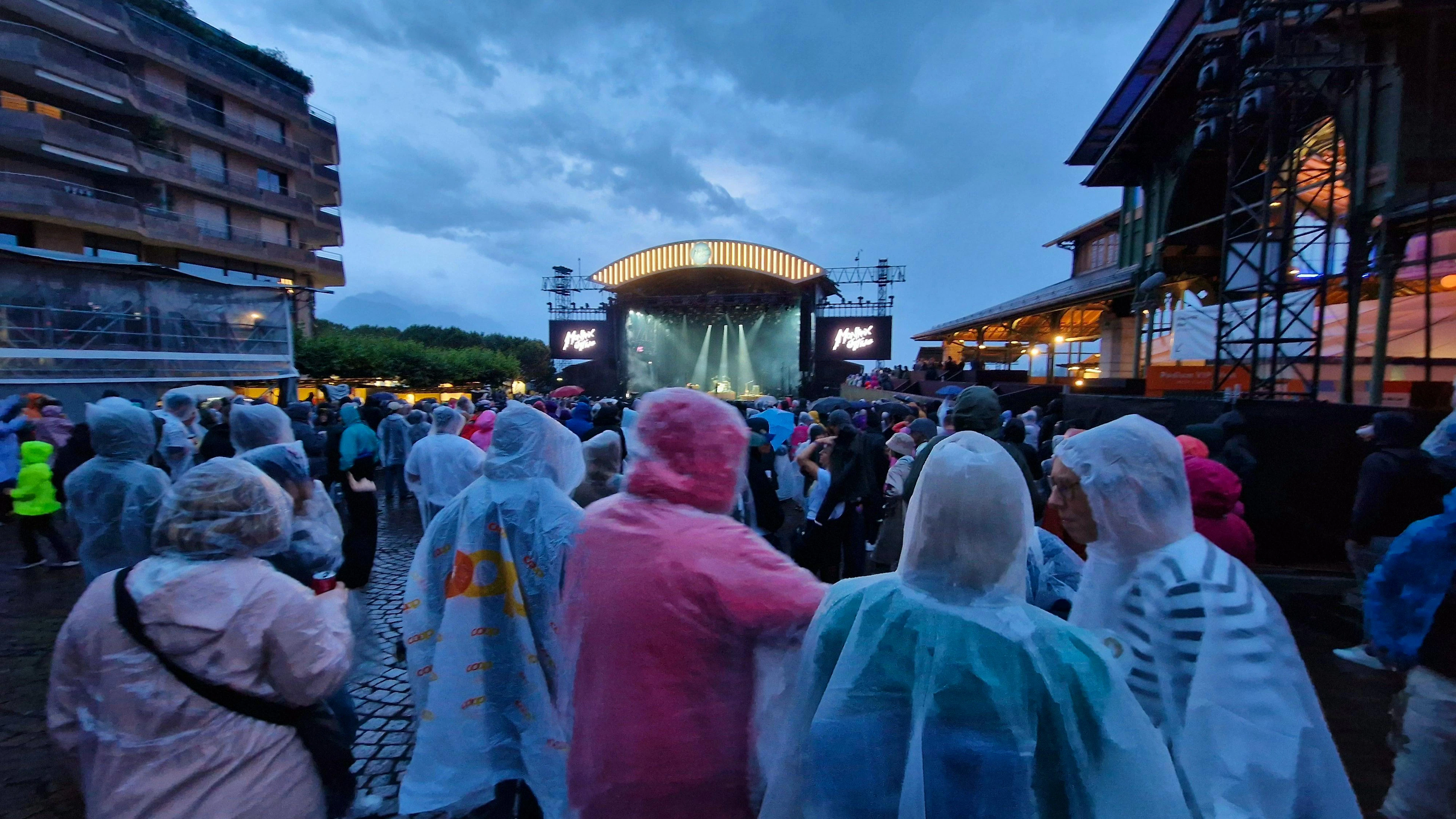 Tout emmitouflés dans leurs pèlerines, les spectateurs attendent sous la pluie l'arrivée de Noah Kahan.