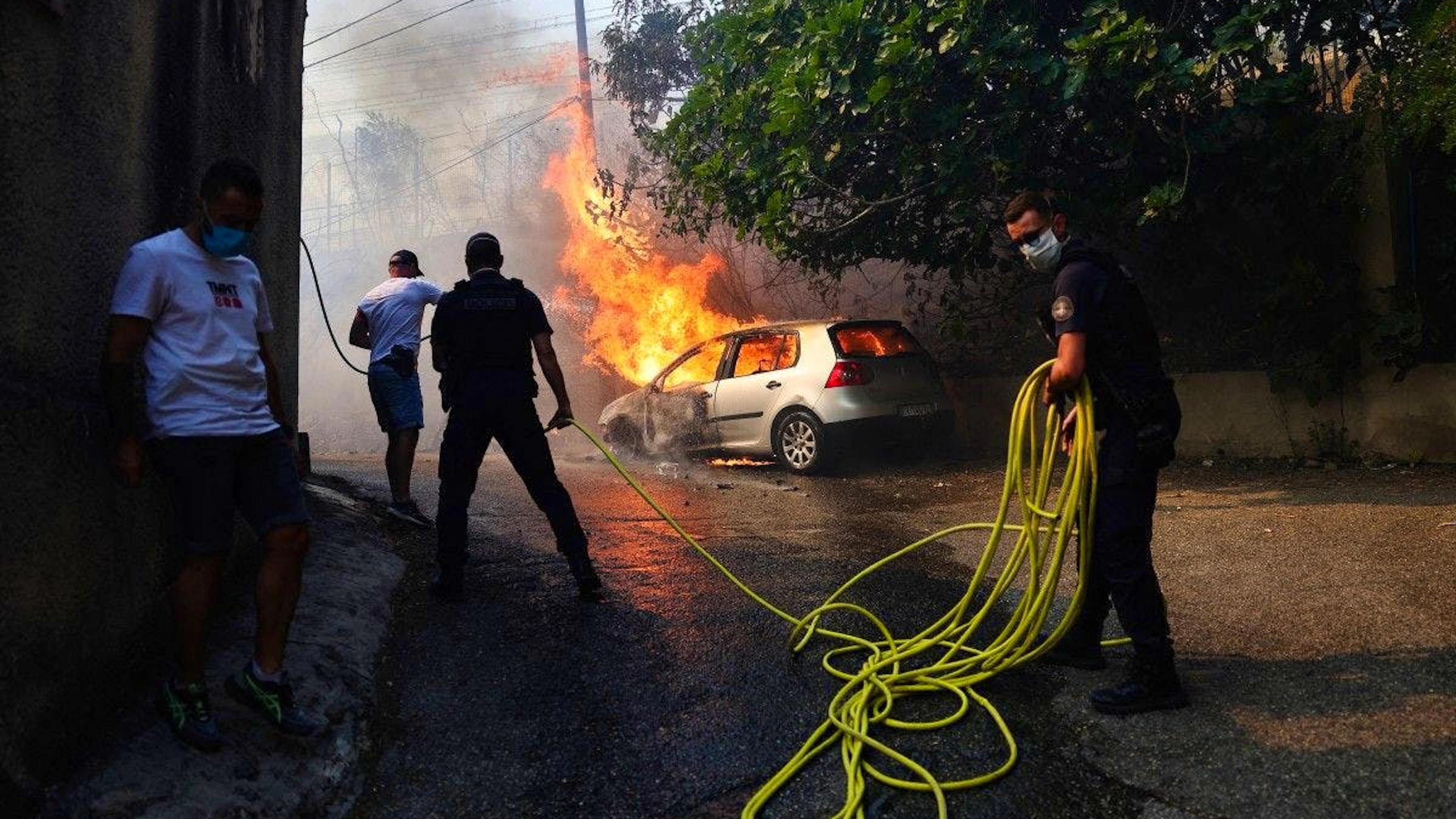 Des policiers tentent d’éteindre une voiture en feu à L’Estaque, un quartier de Marseille, dans le sud de la France, le 8 juillet 2025, alors qu’une fumée provenant d’un incendie de forêt s’élève.