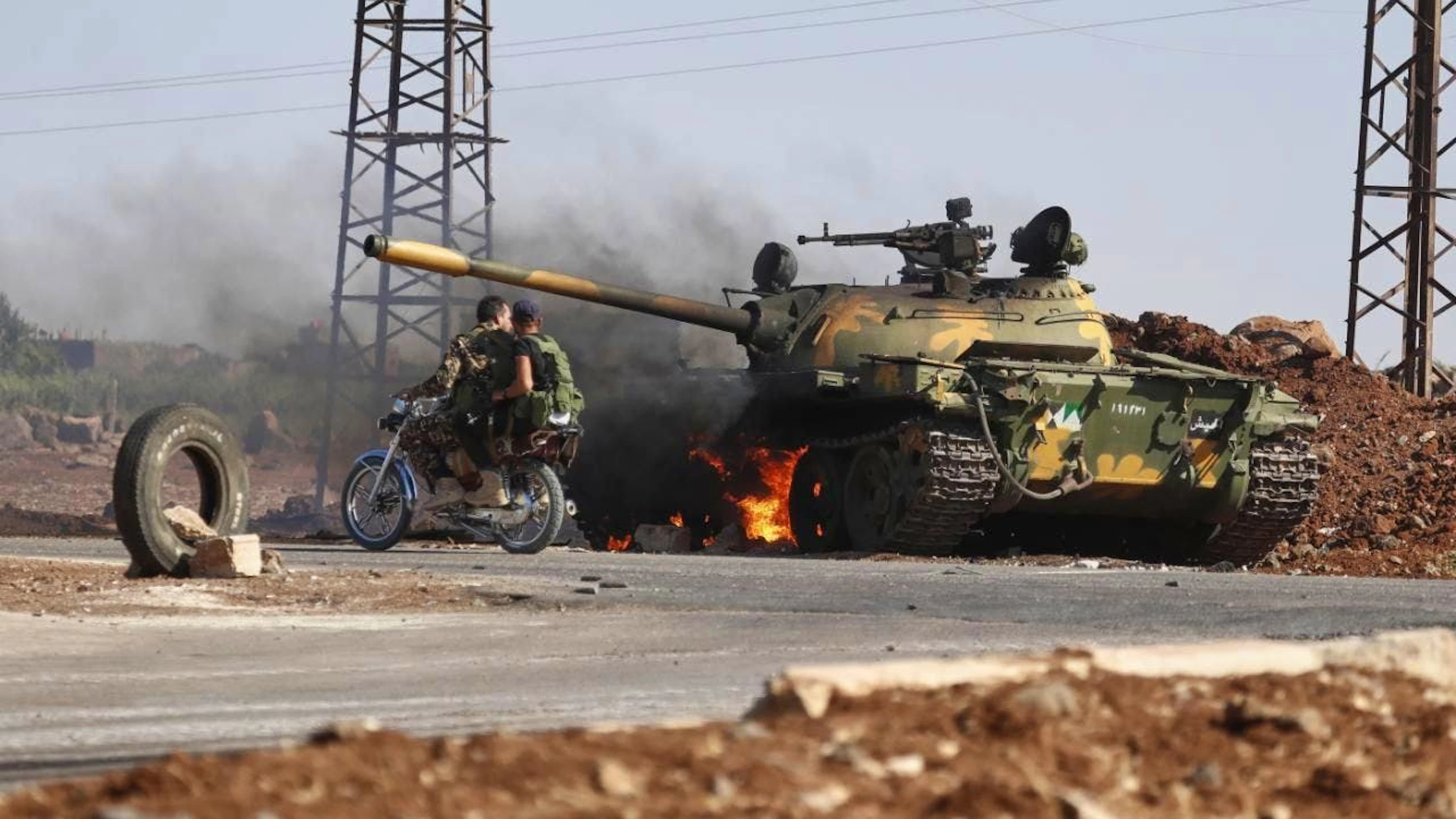 Des soldats du gouvernement syrien à moto passent devant un char en feu à la périphérie de la ville de Soueida (archives).