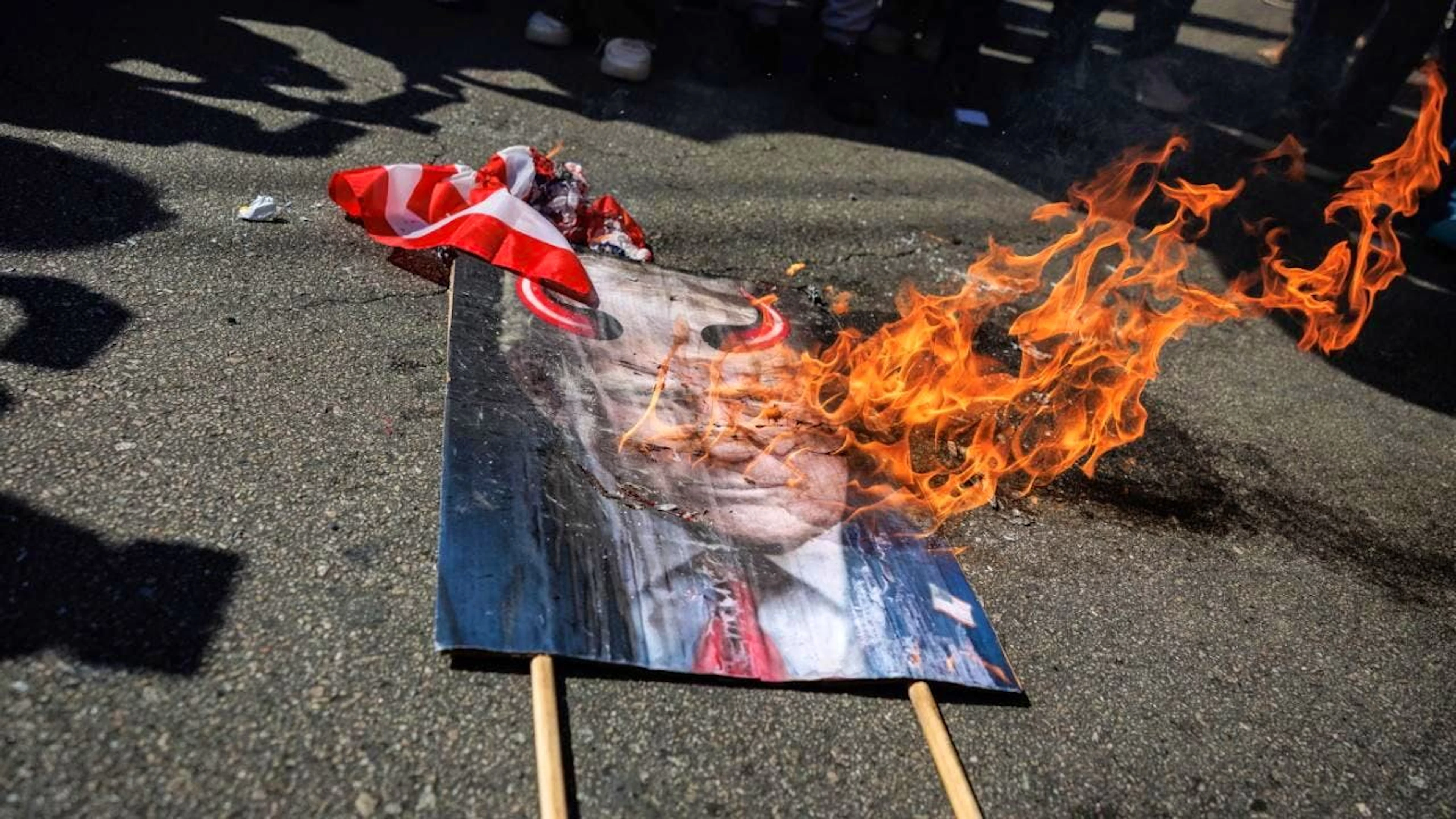 Una bandiera degli Stati Uniti e un cartellone raffigurante l'immagine del presidente Donald Trump vengono dati alle fiamme in segno di pretesta.