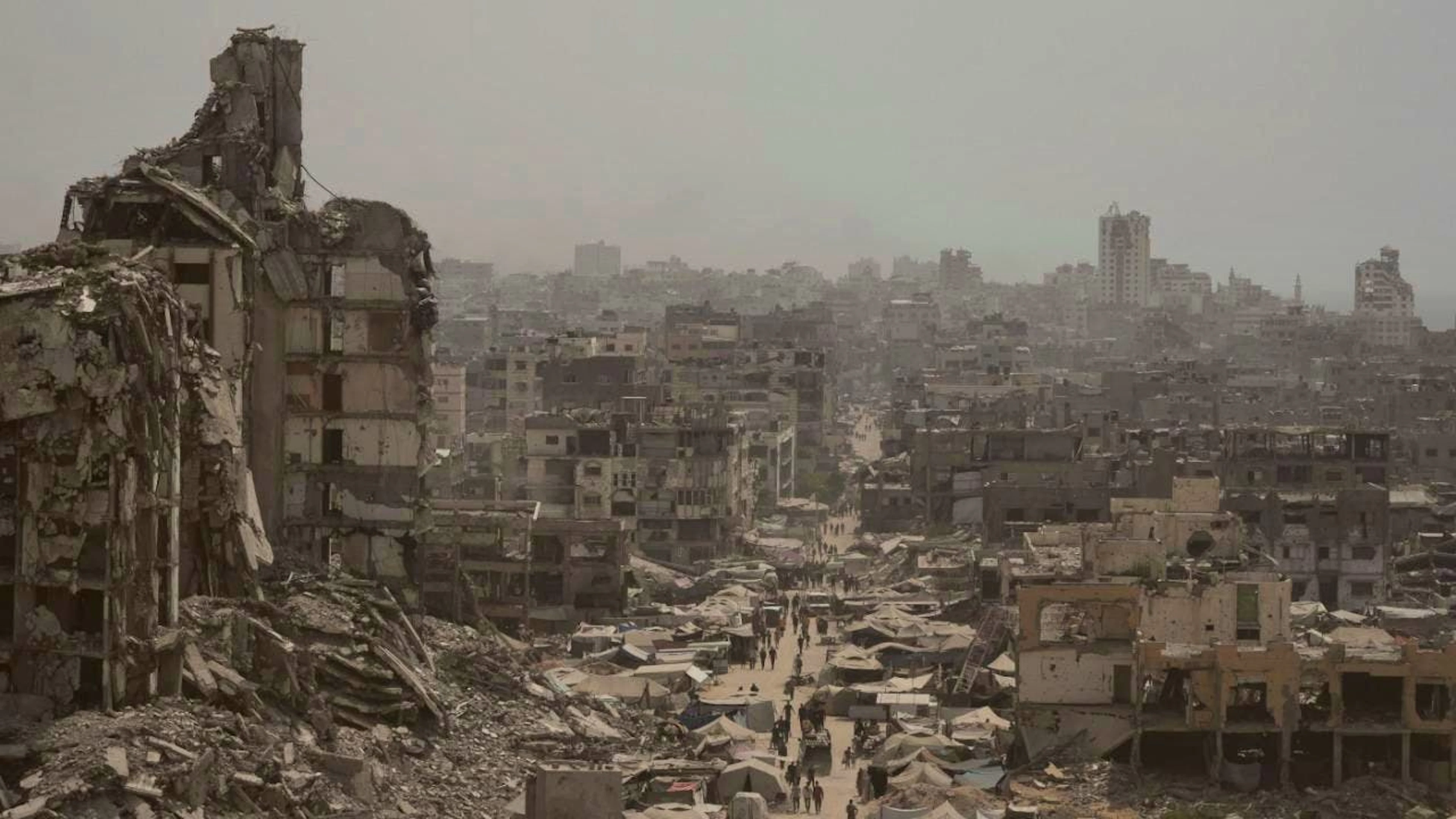 ARCHIV - Menschen gehen eine Straße entlang, die von Gebäuden umgeben ist, die durch israelische Bombardierungen im Gazastreifen zerstört wurden. Foto: Jehad Alshrafi/AP/dpa