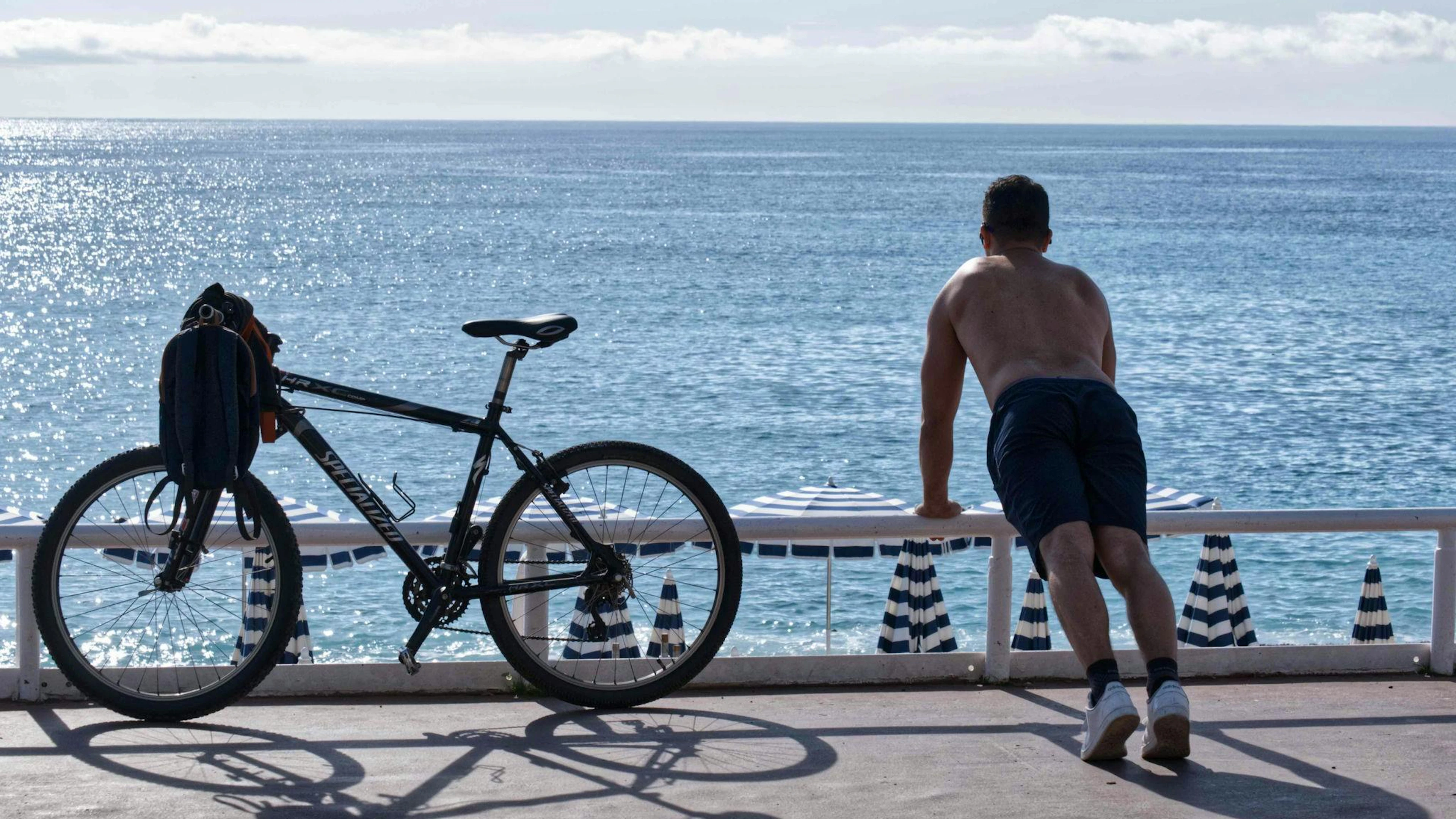 Ein Mann mit nacktem Oberkörper macht am Strand von Nizza neben seinem Fahrrad Übungen. (Archivbild)
