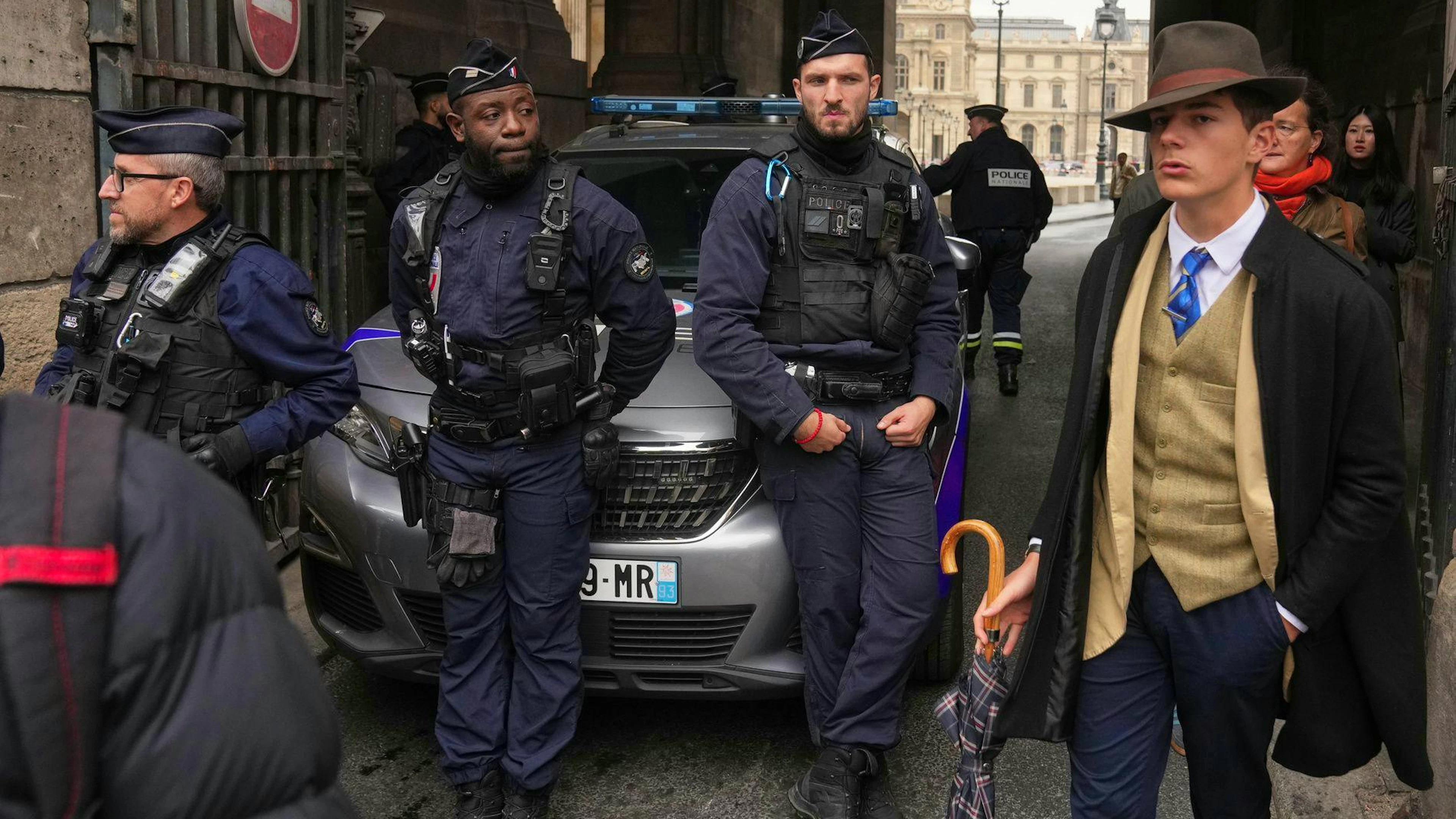 Un jeune homme à chapeau au look chic désuet passant devant des policiers postés devant le Louvre et immortalisés par l'agence de presse AP.