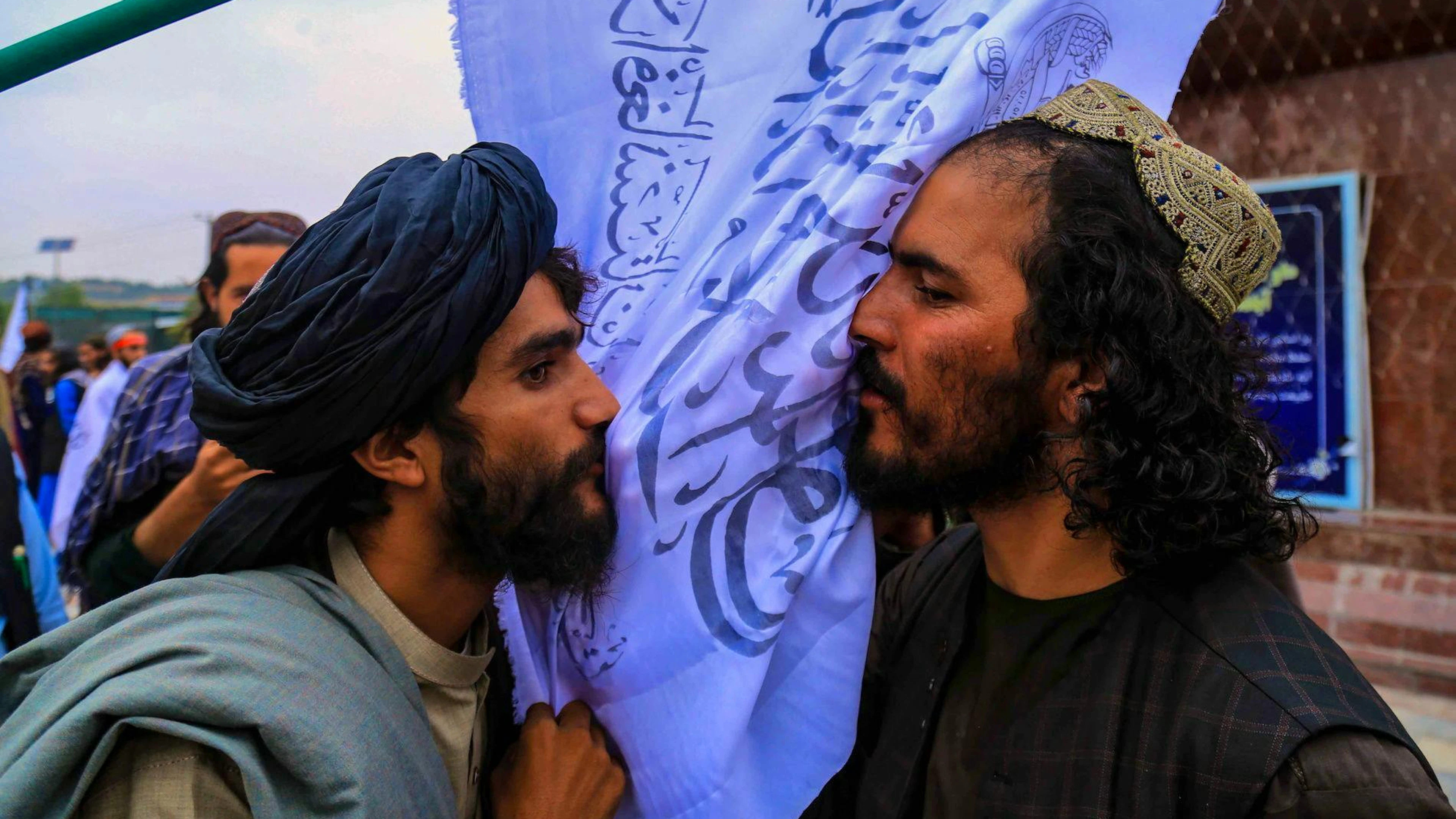 Taliban-Mitglieder küssen bei einer Versammlung nahe dem Gebäude der ehemaligen US-Botschaft in Kabul eine Fahne ihrer Bewegung, um am 15. August 2022 den ersten Jahrestag ihrer Machtübernahme in Afghanistan zu feiern.