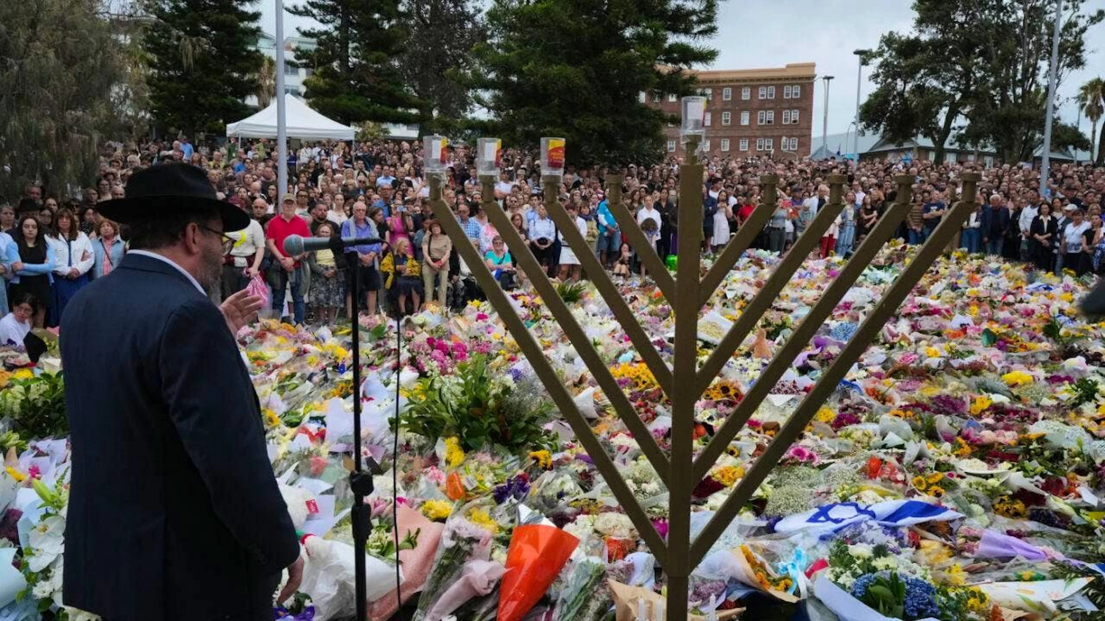 Strage a Bondi Beach: la polizia annuncia che un attentatore si è risvegliato dal coma. Nella foto il rabbino Motti Feldman parla davanti al memoriale per le 15 vittime e gli oltre 40 feriti.