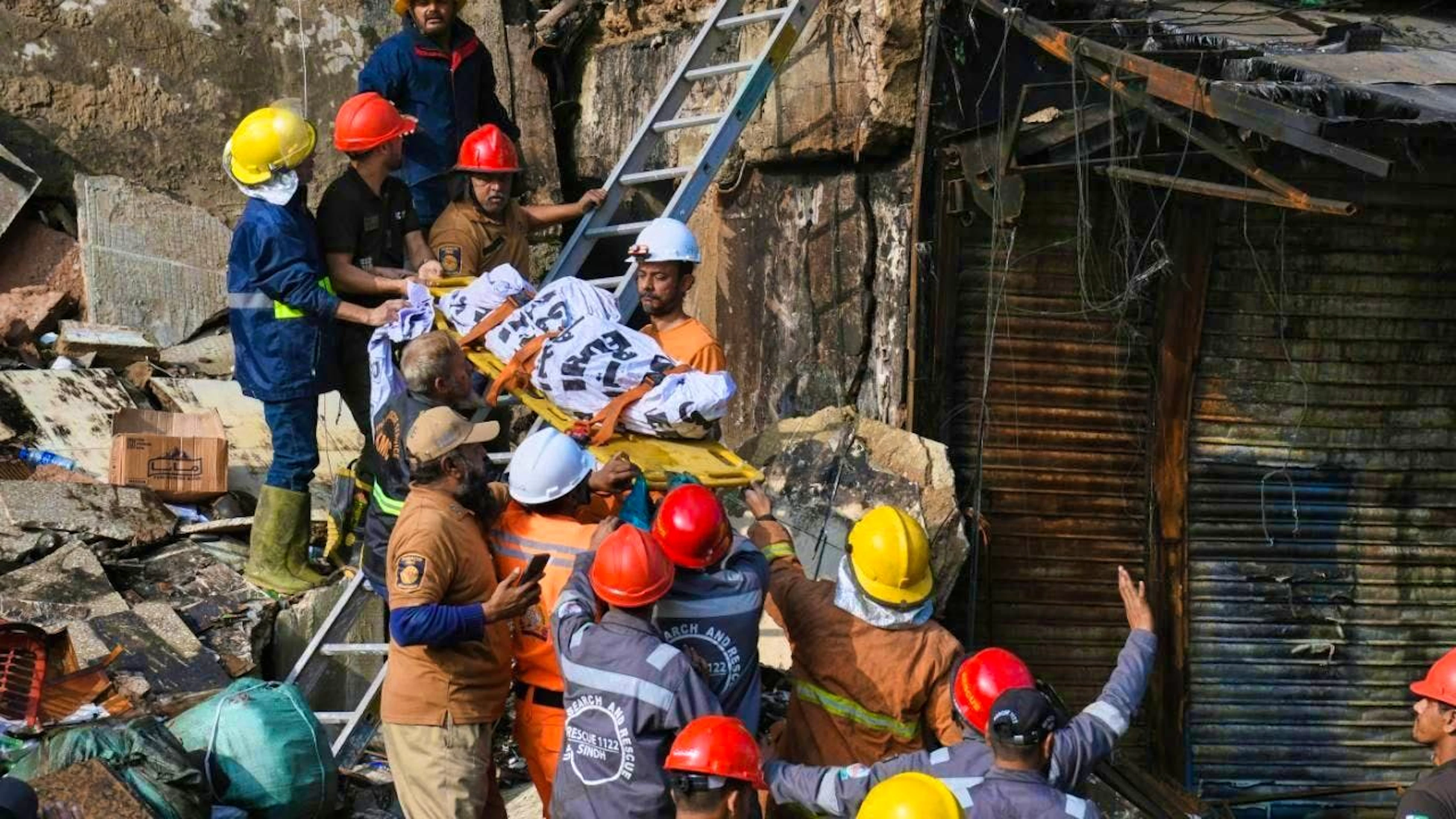 Firefighters carry a body after recovering it from the rubble of a burnt down building of a multi-storey shopping mall after a major fire. Photo: Ali Raza/AP/dpa