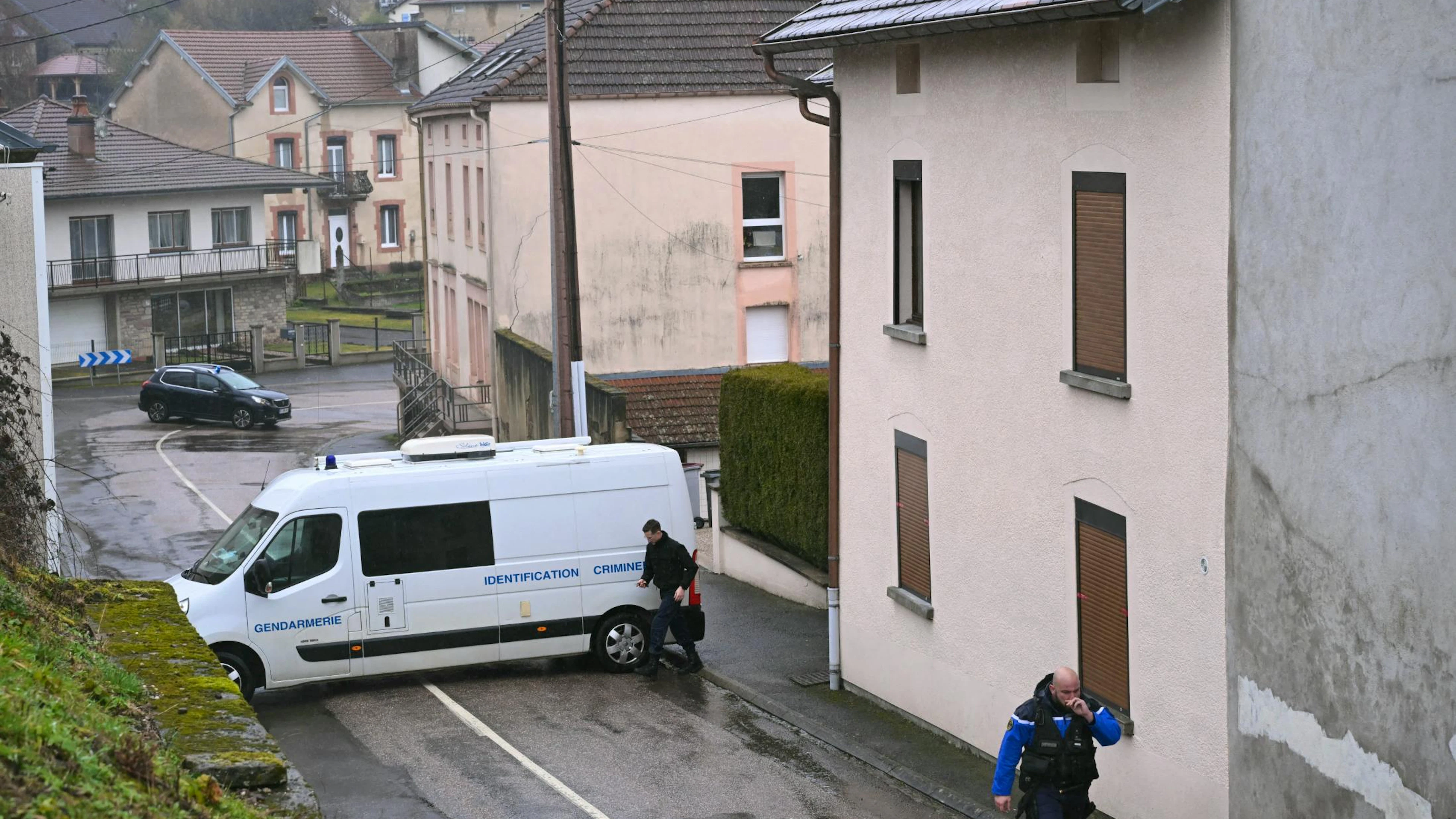 Un gendarme passe devant un véhicule appartenant à l'unité d'identification criminelle de la gendarmerie française lors d'une perquisition policière dans la maison (à droite) où les corps de deux nourrissons ont été découverts dans un congélateur à Ailleviller-et-Lyaumont, dans l'est de la France, le 18 février 2026.