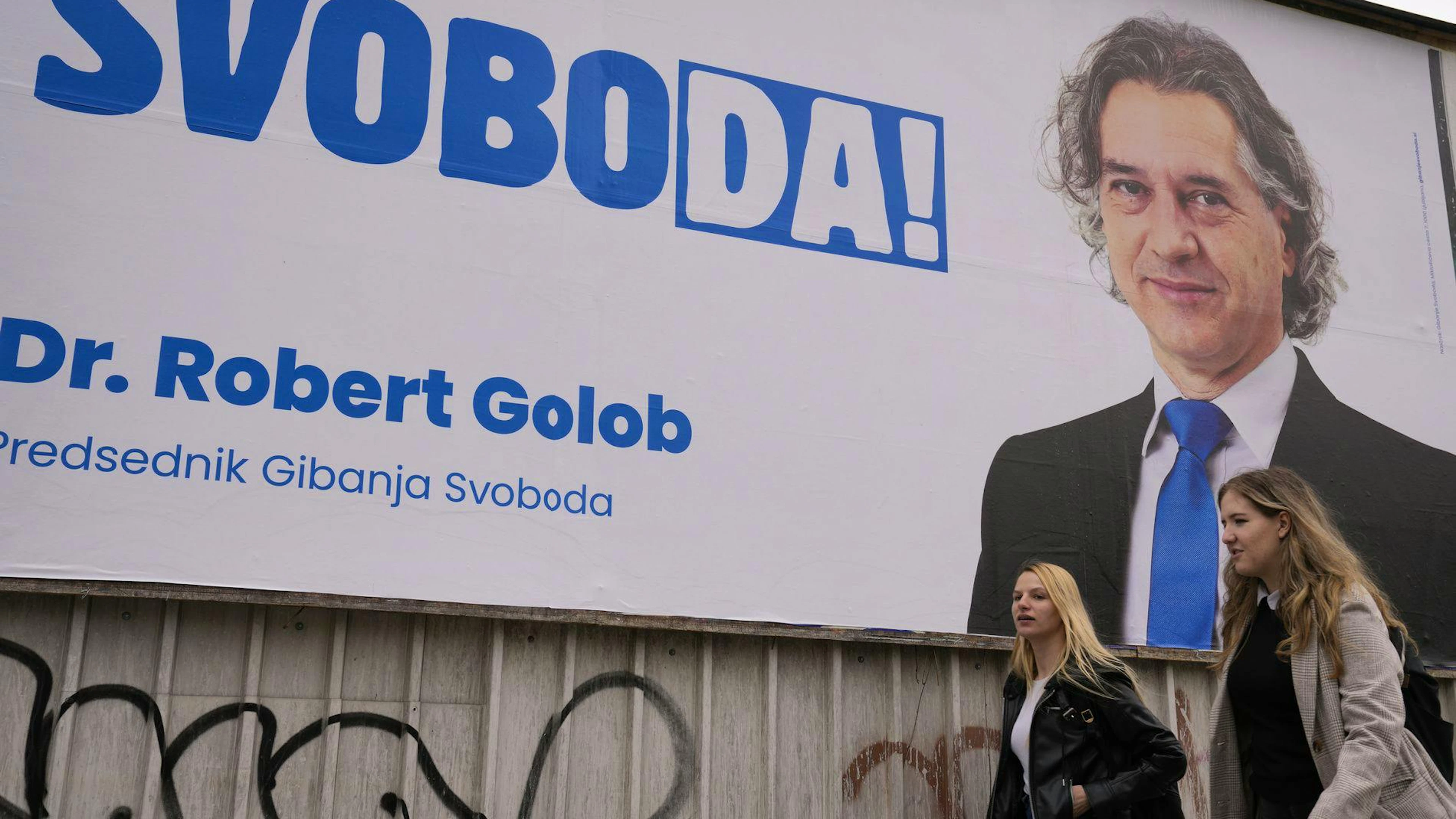 Des piétons passent devant une affiche électorale de Robert Golob, candidat libéral, à Ljubljana, en Slovénie, le jeudi 21 avril 2022. Le scrutin de dimanche 24 avril en Slovénie se déroulera dans un contexte de divisions politiques accrues au sein de ce petit pays alpin de 2 millions d'habitants. (Photo AP/Darko Bandic)