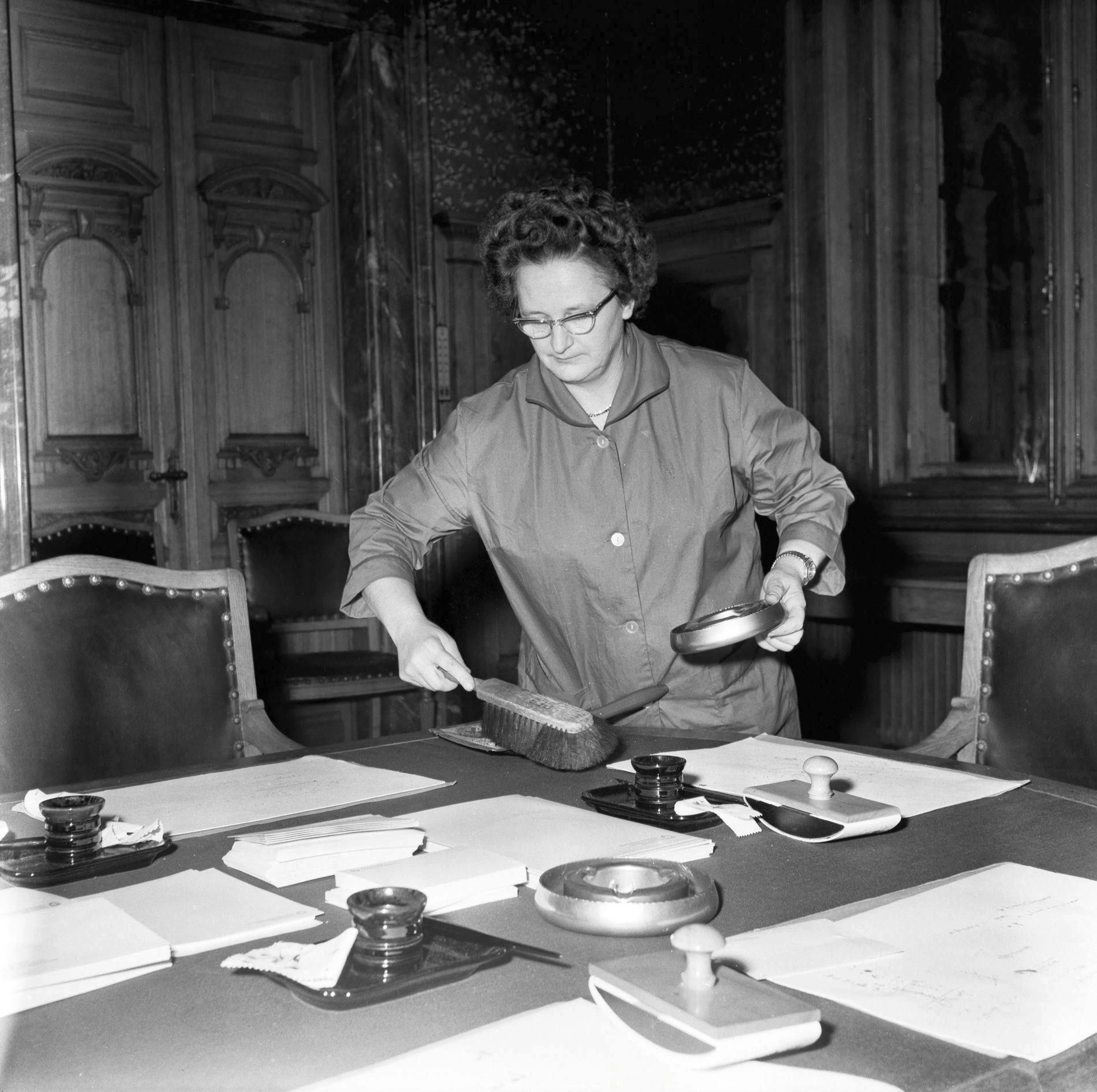 A cleaner wipes the tables and empties the ashtrays in the Federal Palace in Bern after the end of the session, taken in 1963.