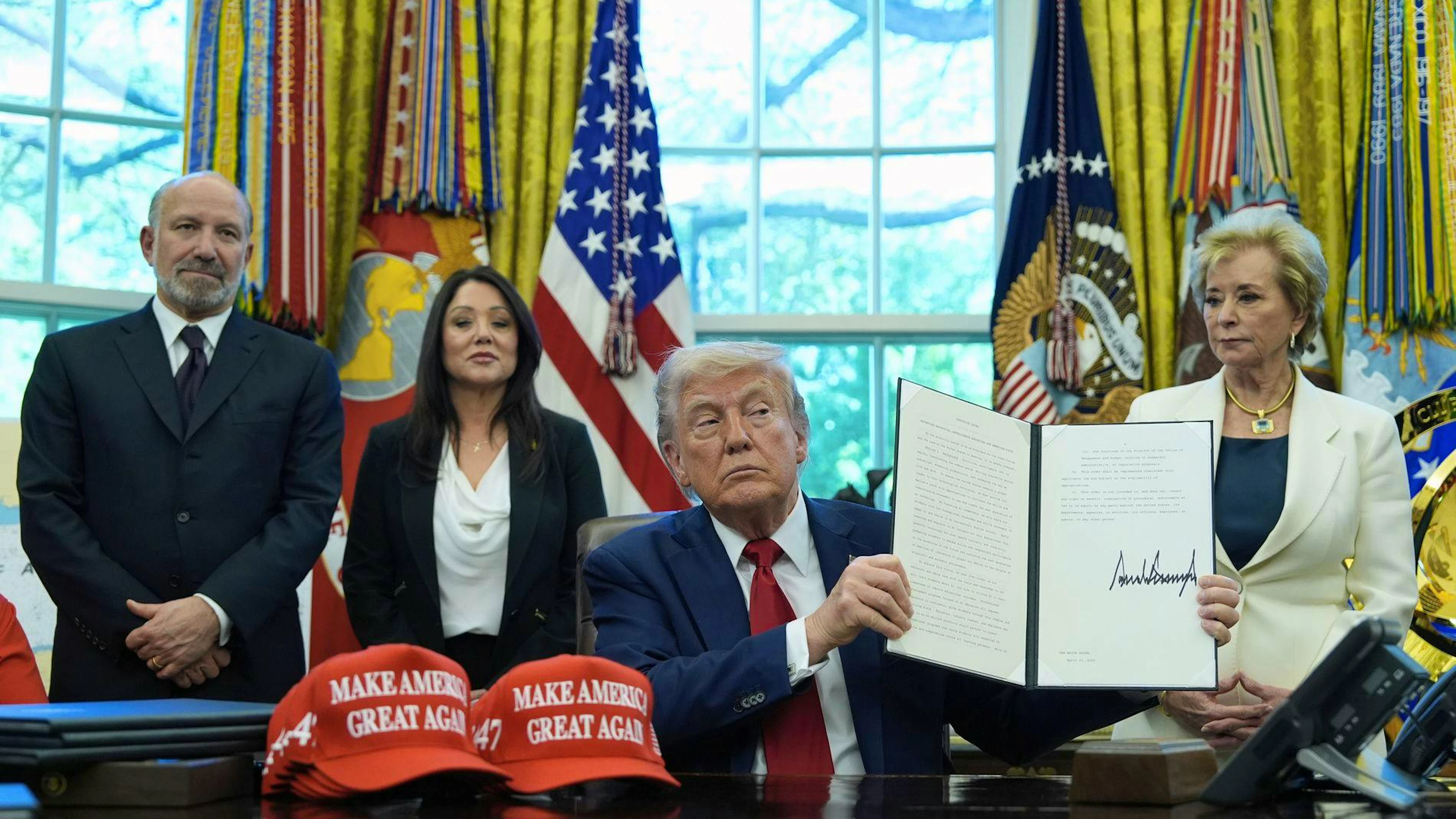 Donald Trump tiene in mano un decreto presidenziale in materia di istruzione nello Studio Ovale della Casa Bianca, sotto lo sguardo del segretario al Commercio Howard Lutnick (a sinistra), della segretaria al Lavoro Lori Chavez-DeRemer (dietro al centro) e della segretaria all'Istruzione Linda McMahon.
