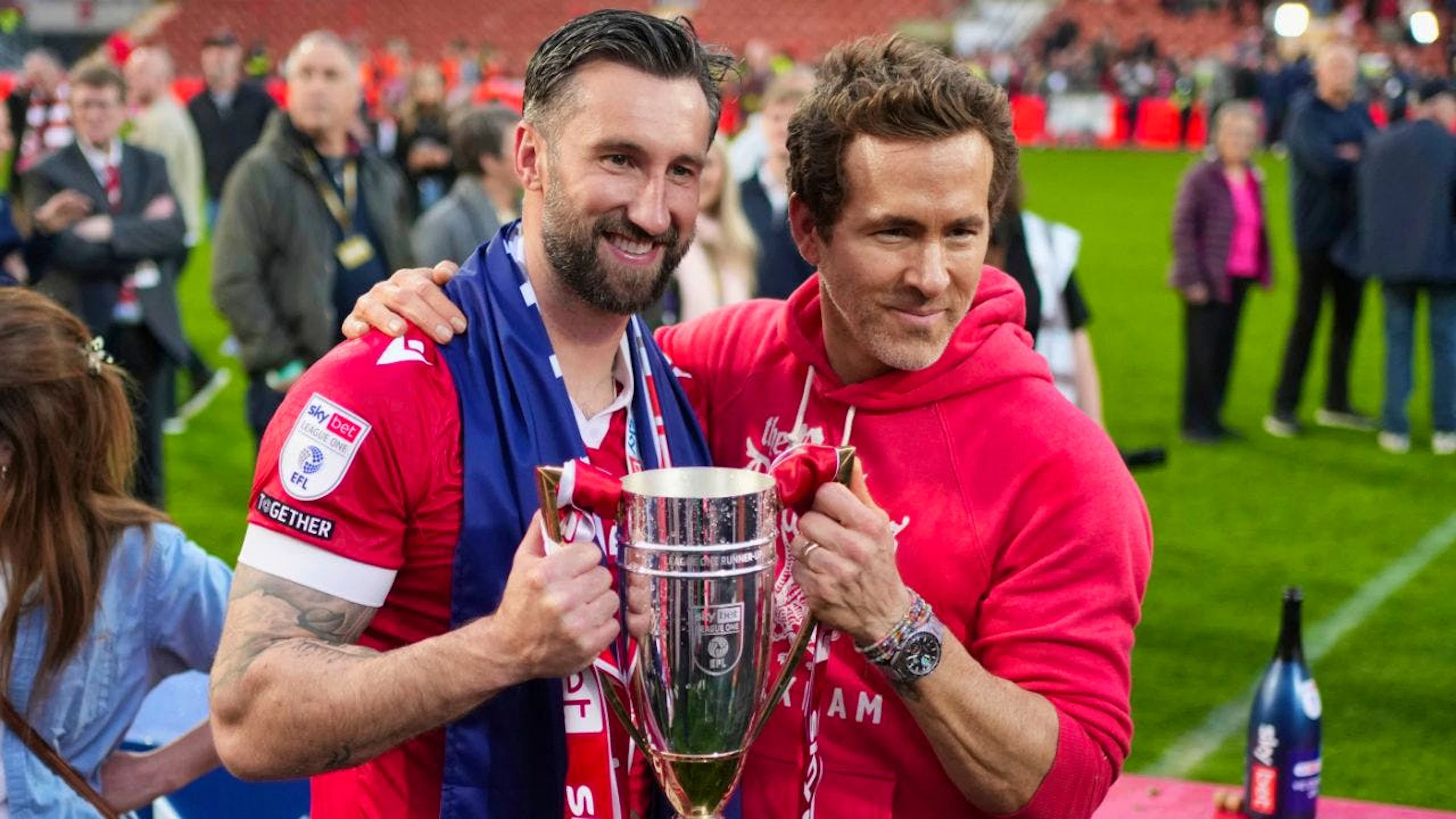 Der Hollywood-Star Ryan Reynolds, der seit gut fünf Jahren Co-Besitzer des AFC Wrexham ist, und Spieler Ollie Palmer (links) posieren nach dem Aufstieg in die Championship in der vergangenen Saison mit dem Pokal