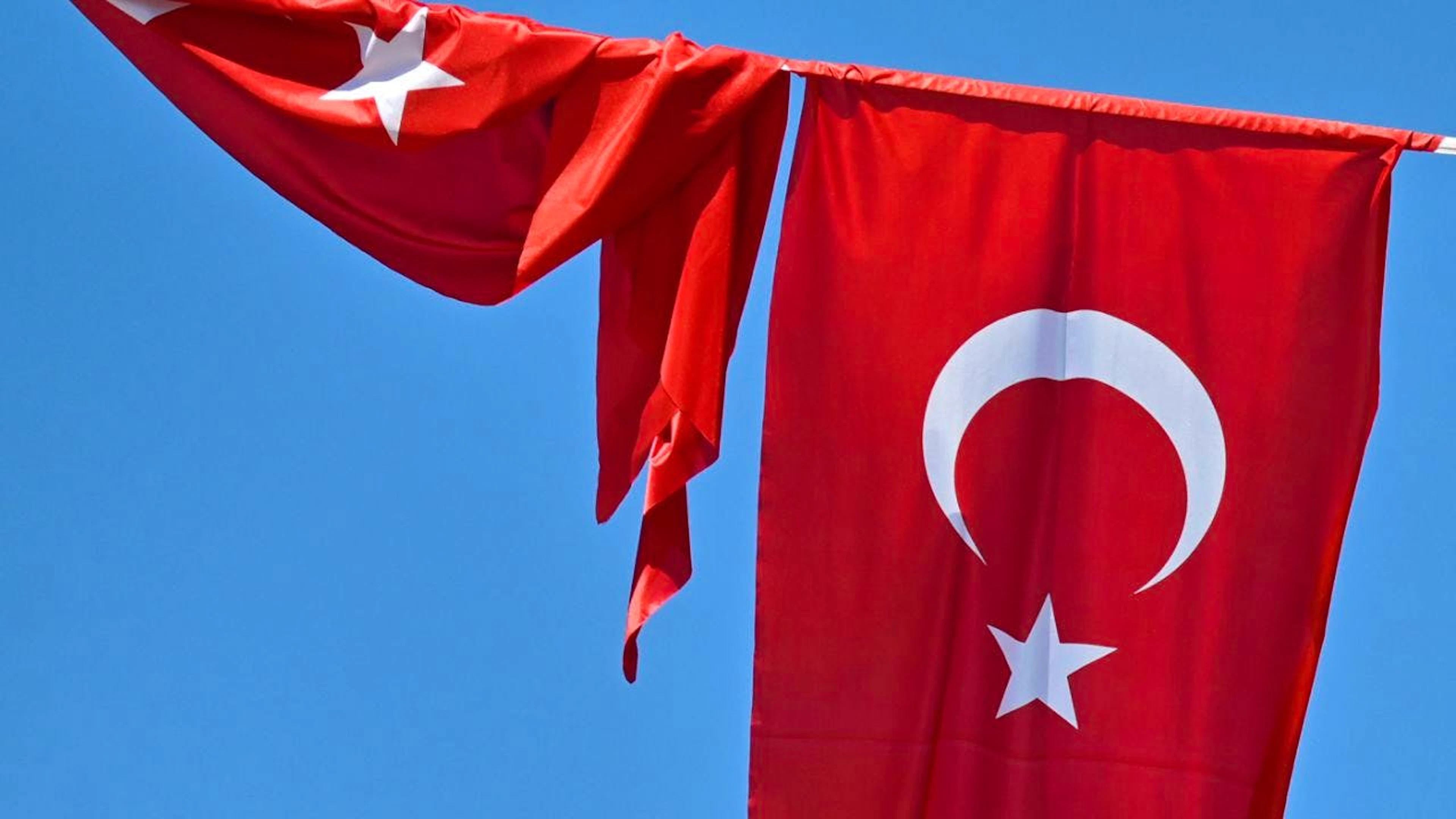 ARCHIV – Eine türkische Flagge weht vor blauem Himmel im Wind, während eine zweite Flagge aufgewickelt daneben hängt. Foto: Anna Ross/dpa/Symbolbild