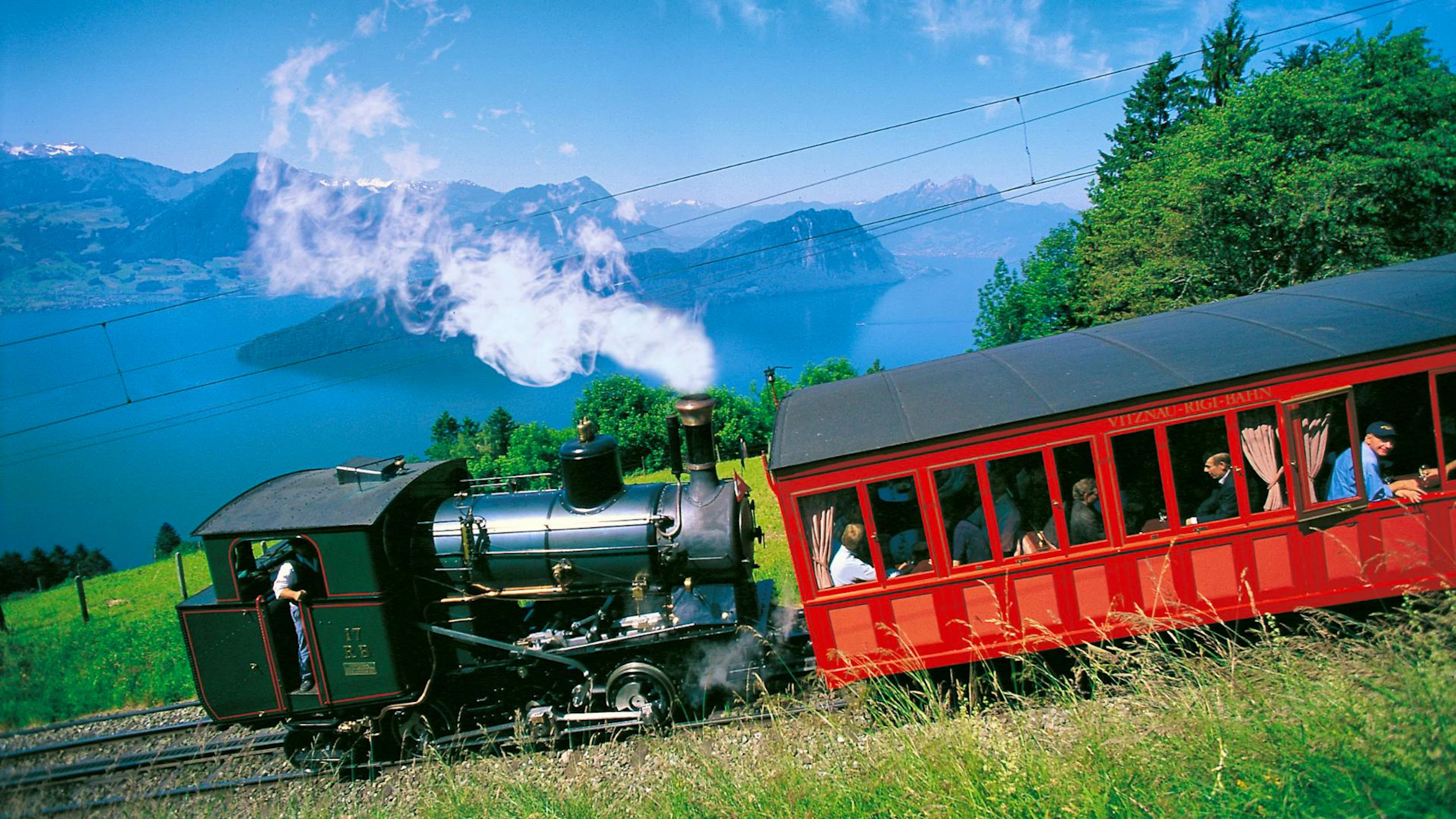 Die historische Rigi-Bahn, Europas erste Bergbahn, fährt mit ihrer Dampflokomotive hoch über dem Vierwaldstättersee dem Gipfel entgegen.