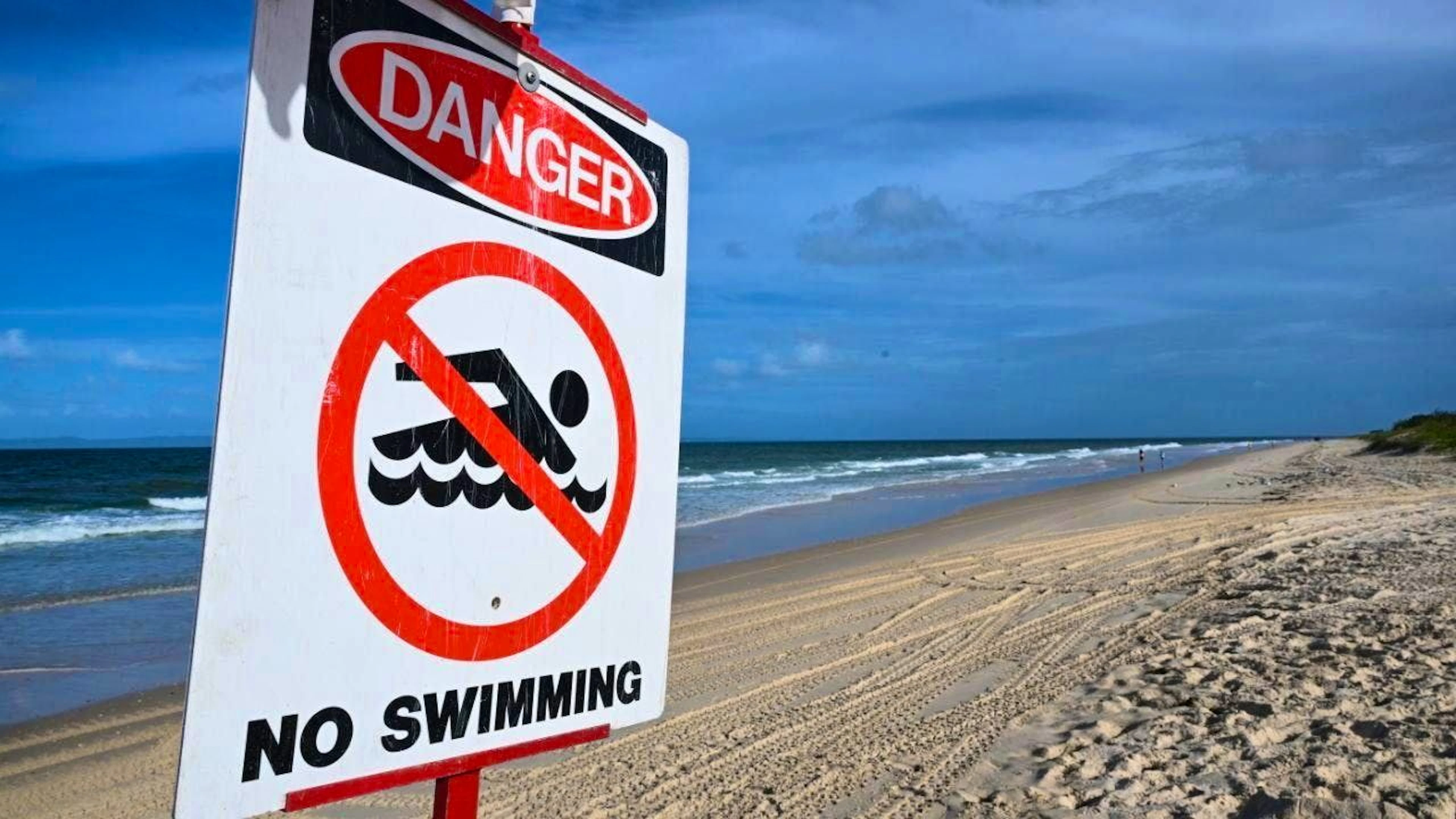 ARCHIVE - A sign reading "Danger - No Swimming" stands on Woorim Beach on Bribie Island. Photo: Darren England/AAP/dpa