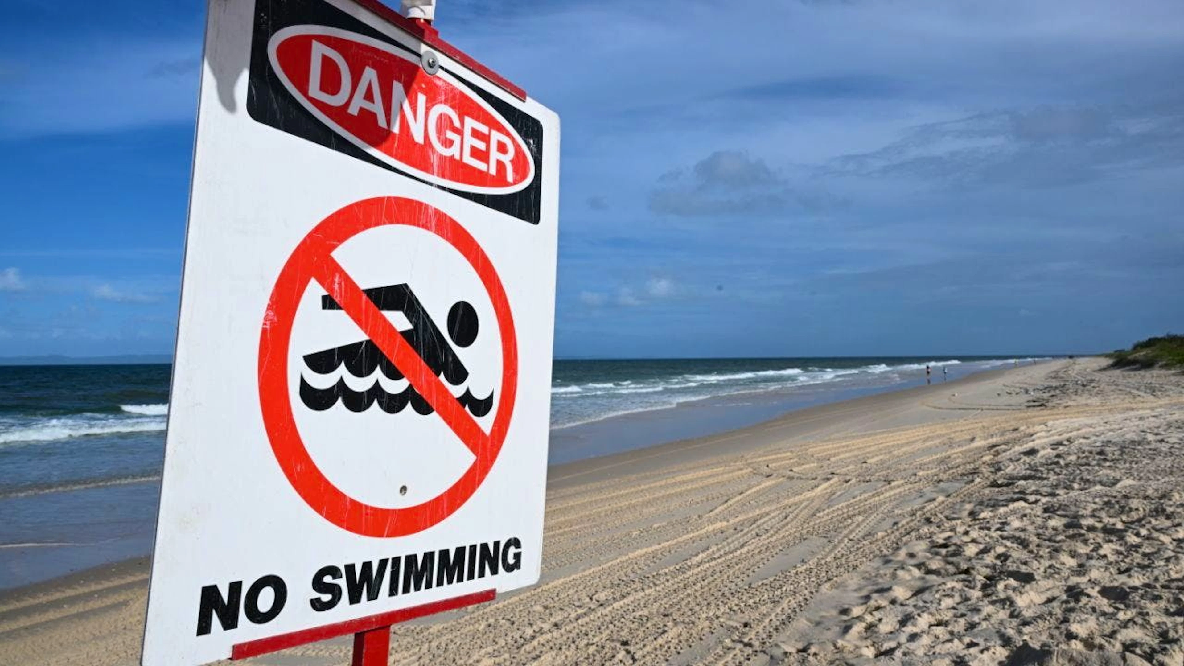 ARCHIV – Ein Schild mit der Aufschrift «Gefahr – Schwimmen verboten» steht an dem Strand Woorim Beach auf Bribie Island. Foto: Darren England/AAP/dpa