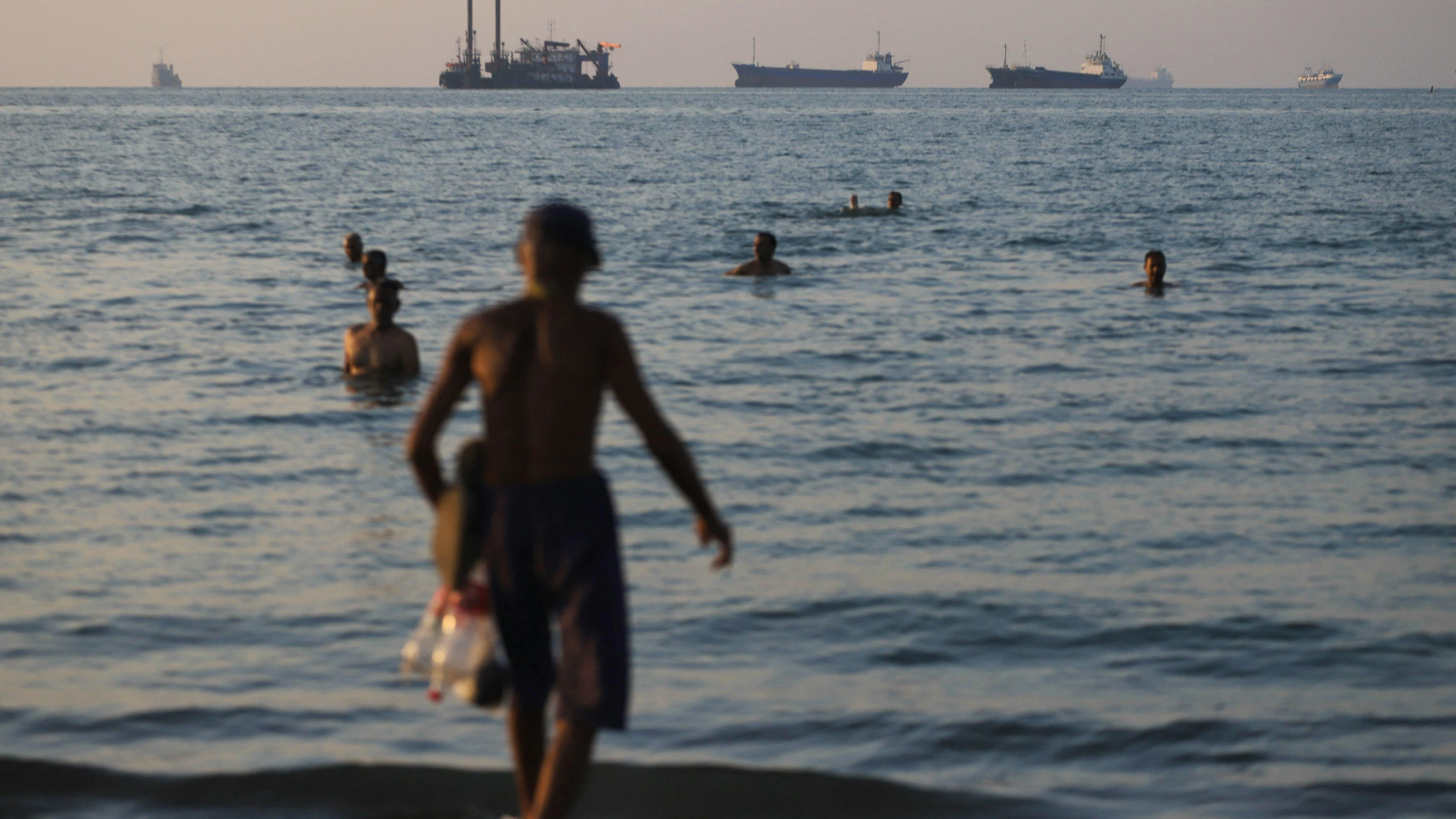 Des habitants se baignent dans le détroit d'Ormuz, au large de Bandar Abbas, tandis que des navires marchands et cargos sont à l'ancre. La photo a été prise le 8 juin 2026, alors que les tensions entre l'Iran et Israël restaient vives malgré un cessez-le-feu fragile. (AFP)