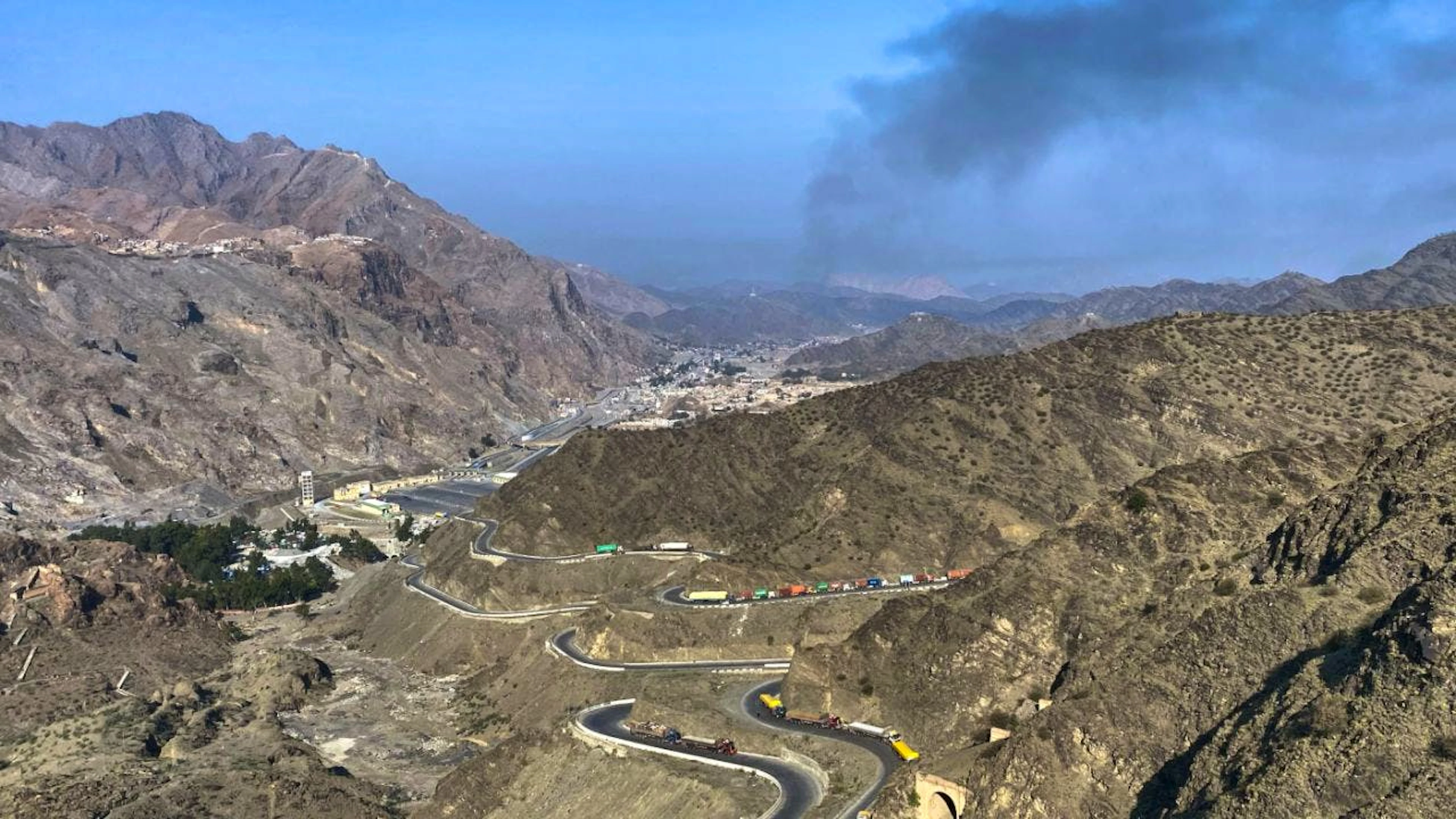 ARCHIV – Nach Zusammenstössen zwischen pakistanischen und afghanischen Streitkräften in der Nähe des Grenzübergangs Torkham in Pakistan steigt Rauch von der afghanischen Seite auf, während Lastwagen am Strassenrand geparkt werden. Foto: Maaz Awan/AP/dpa