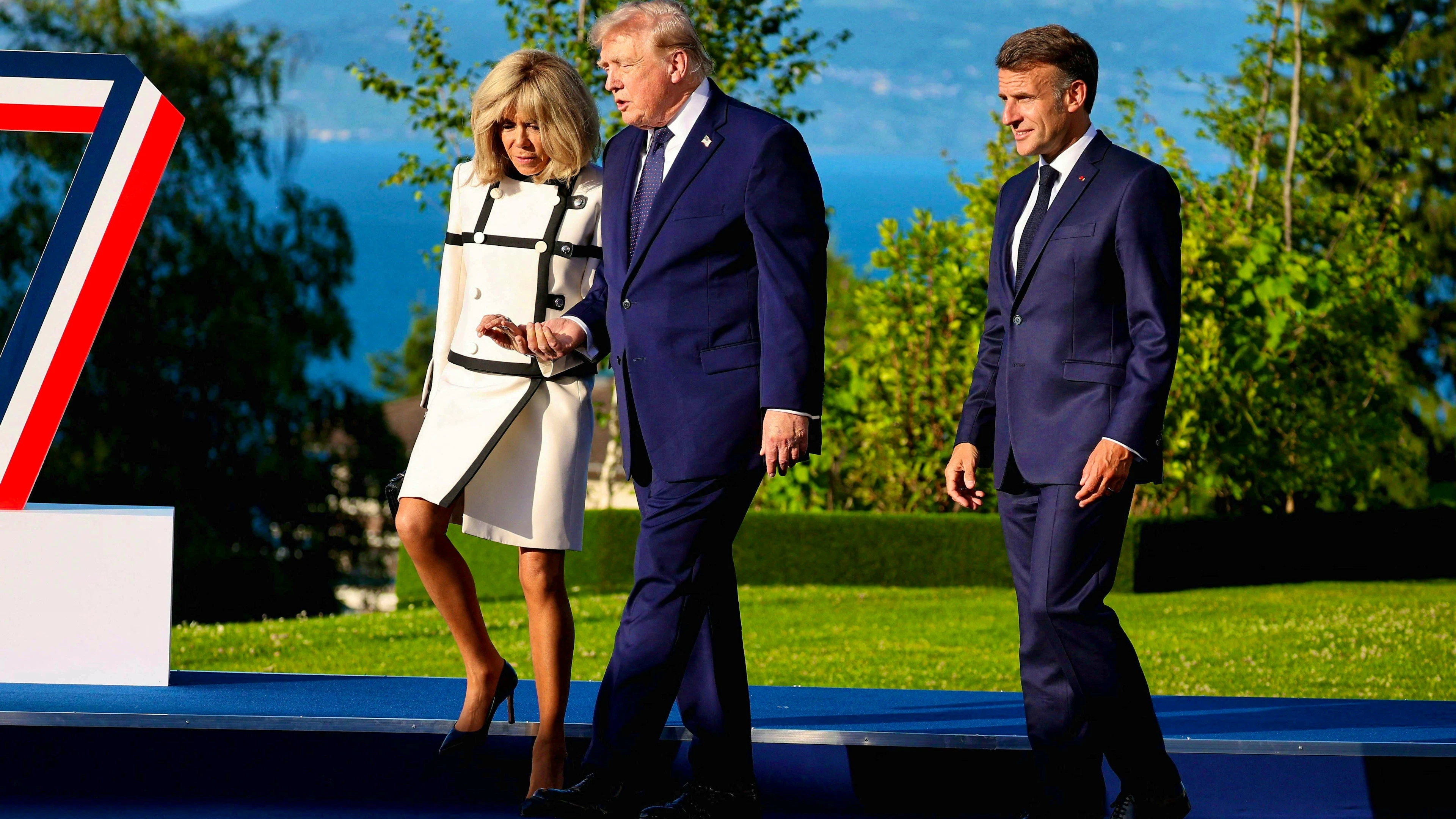 Appena arrivato al G7, Donald Trump trascina Brigitte Macron al suo fianco, sotto lo sguardo divertito del presidente francese.