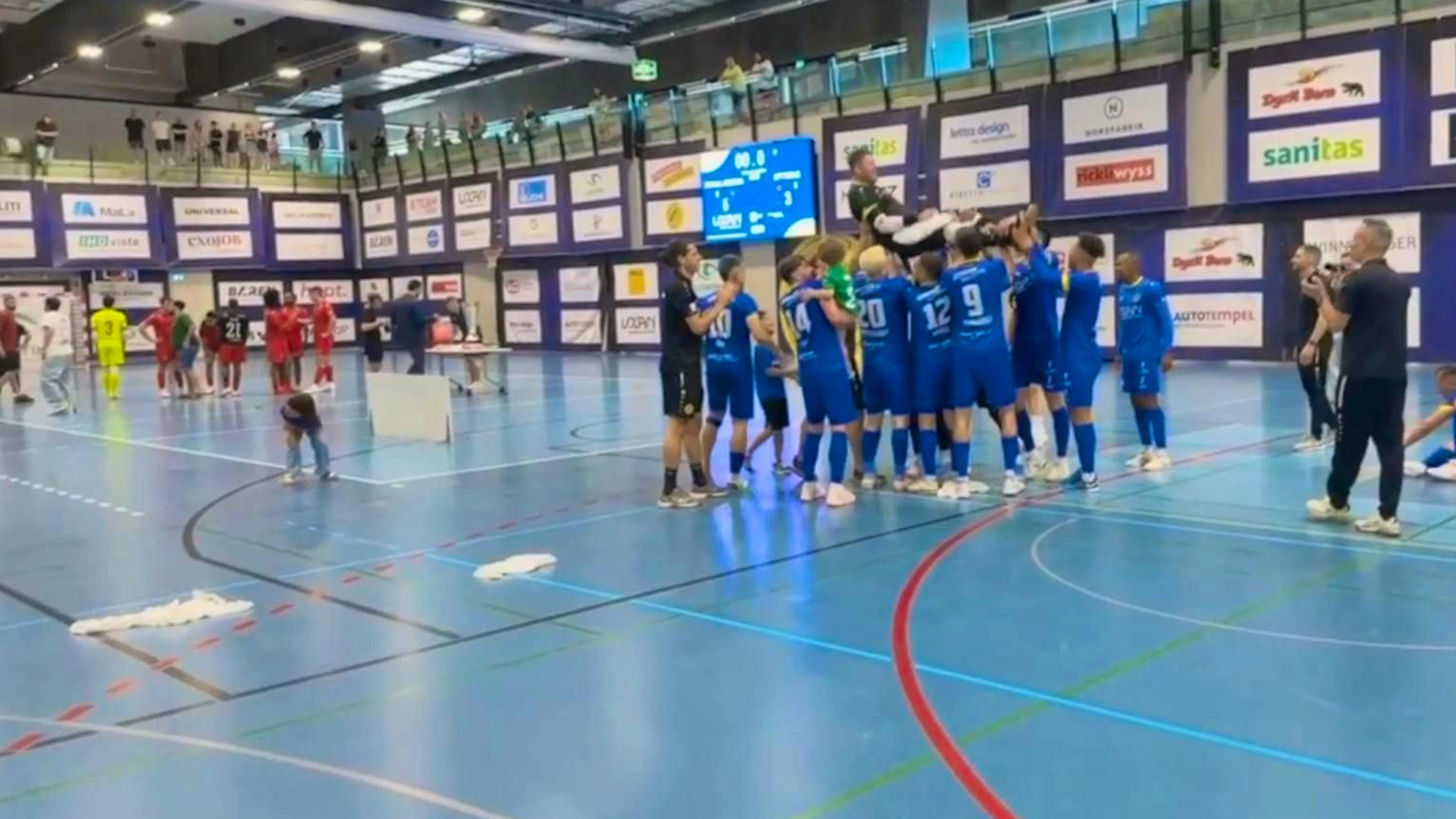 Inside the arena, everything was still going smoothly after the final match. On the right, the celebrating Minerva players in blue jerseys; on the left, a few players from the losing team in red jerseys.