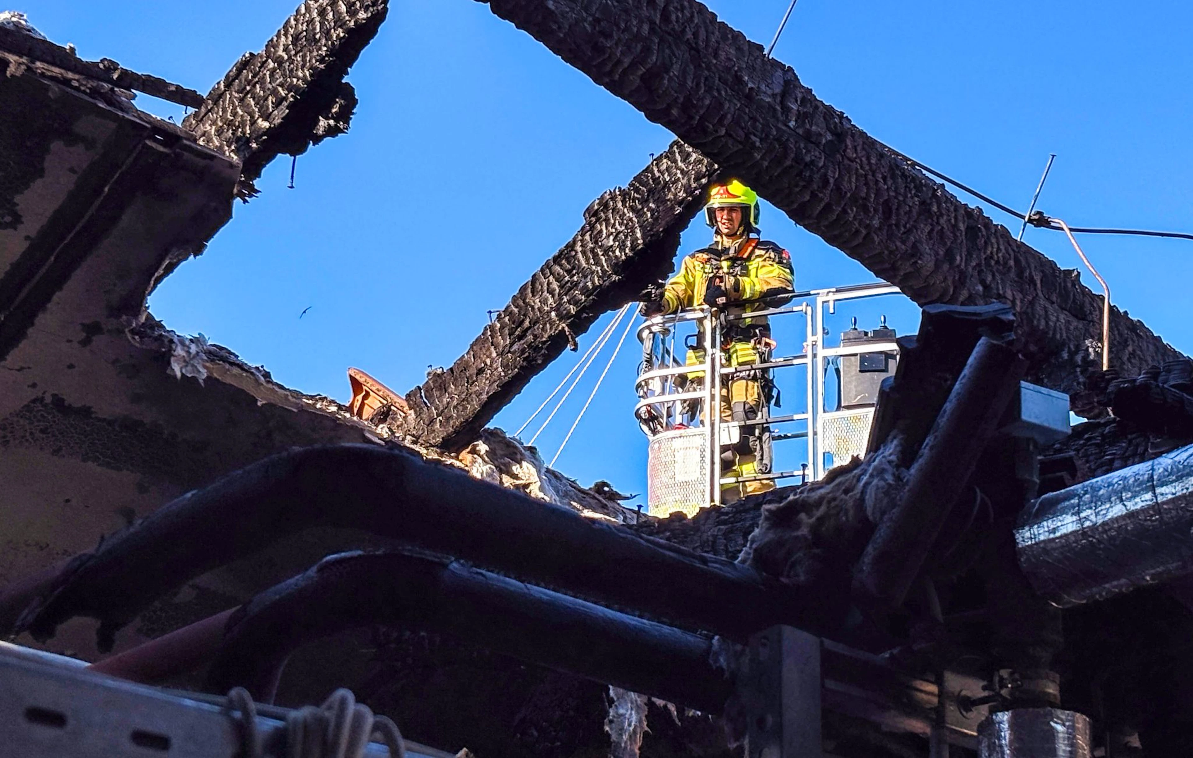 Ein Feuerwehrmann untersucht von einer Drehleiter aus den ausgebrannten Dachstuhl. (Handoutbild)