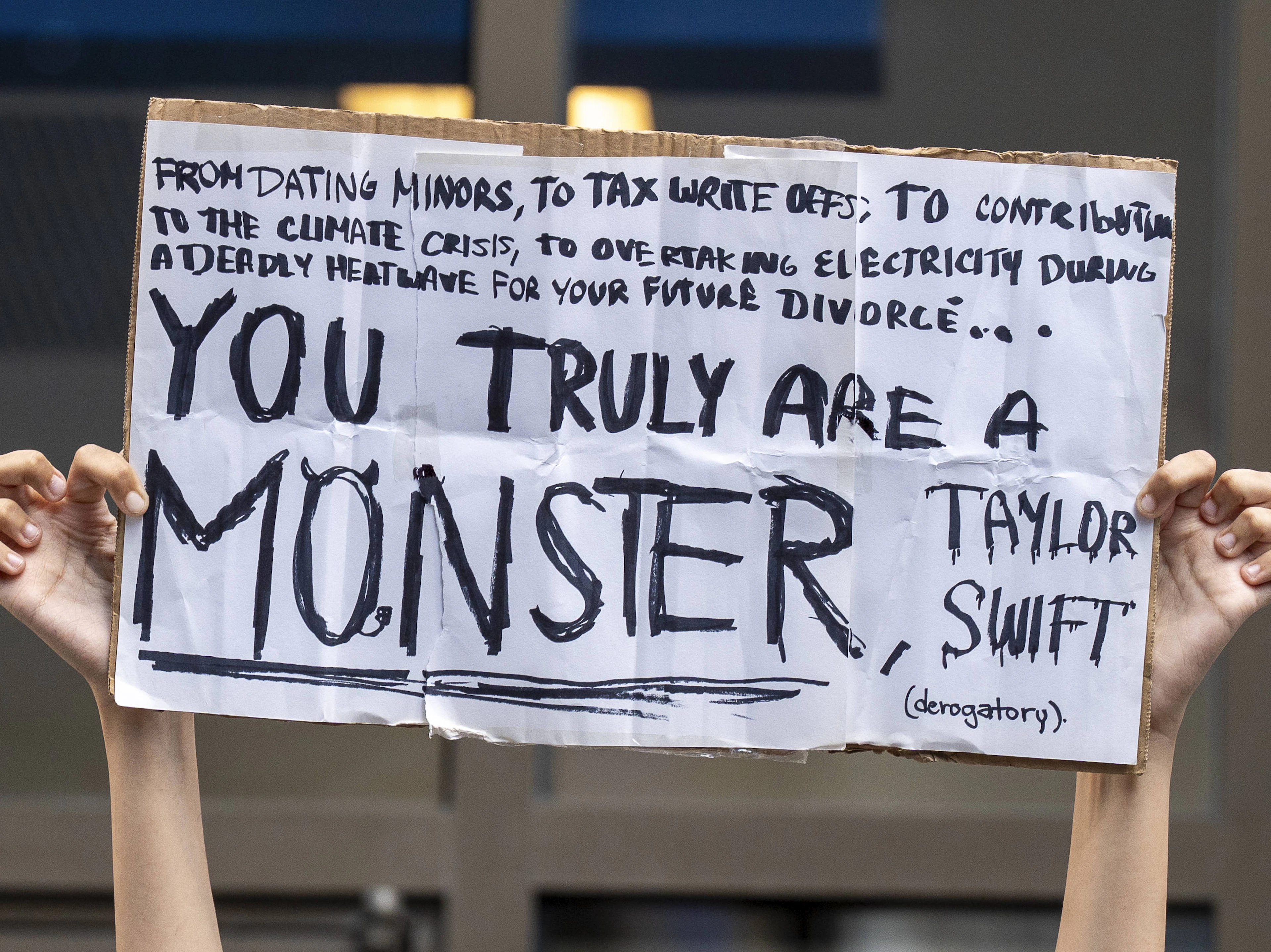 Eine Demonstrantin hält ein Schild hoch, auf dem Taylor Swift scharf kritisiert wird. Die Vorwürfe reichen von ihrem Privatleben bis zu ihrem CO₂-Fussabdruck und zeigen, wie polarisiert die Debatte um den Popstar geführt wird.