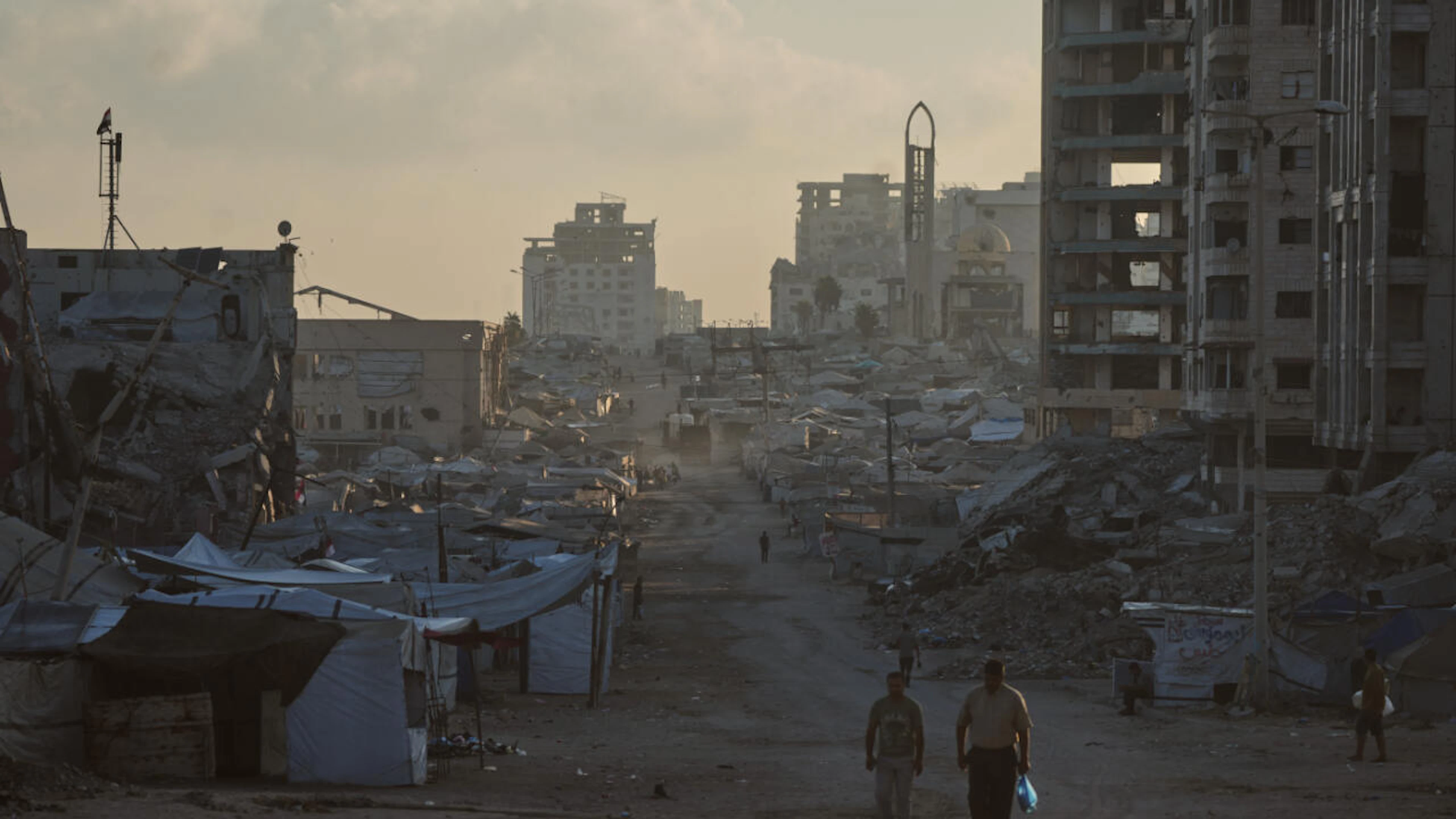 ARCHIV – Palästinenser gehen in Gaza eine Strasse entlang, die von Gebäuden gesäumt ist, die bei israelischen Militärangriffen während des Krieges zwischen Israel und der Hamas zerstört wurden. Foto: Jehad Alshrafi/AP/dpa