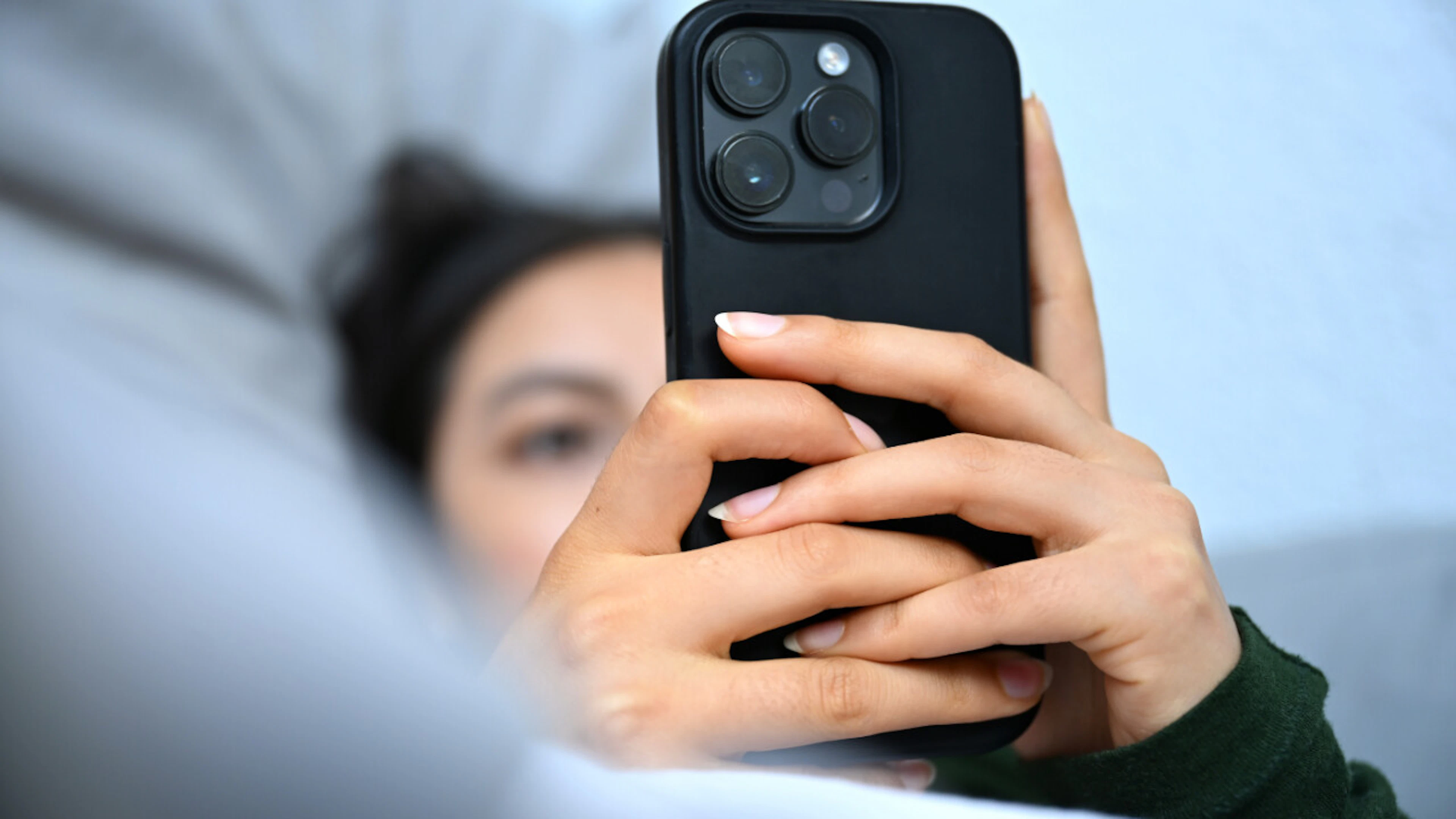 A young woman is lying on the couch with her cell phone, looking at the screen.