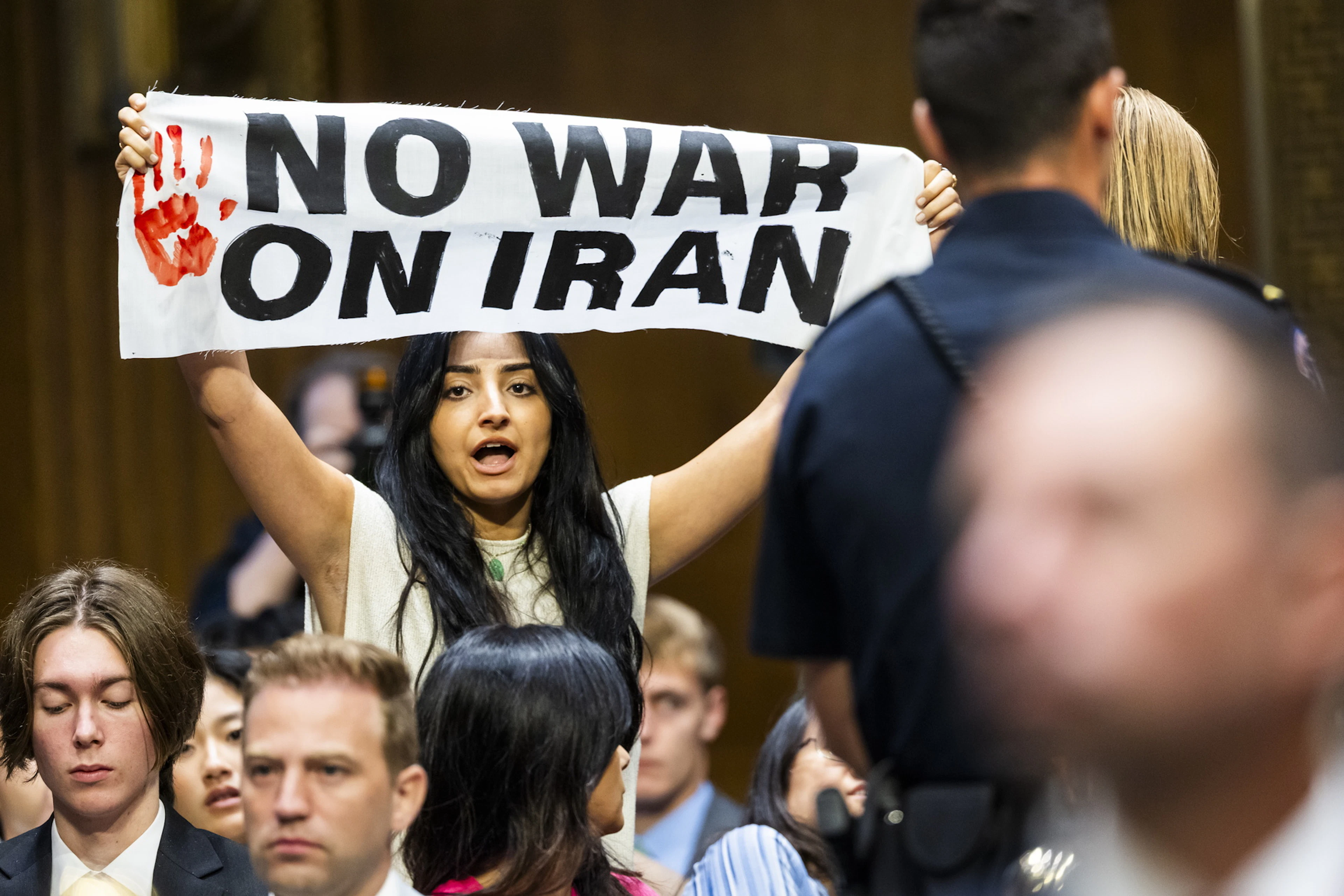 Ein Antikriegsdemonstrant demonstriert gegen den Irankrieg, während US-Verteidigungsminister Hegseth über das Kriegsbudget spricht.